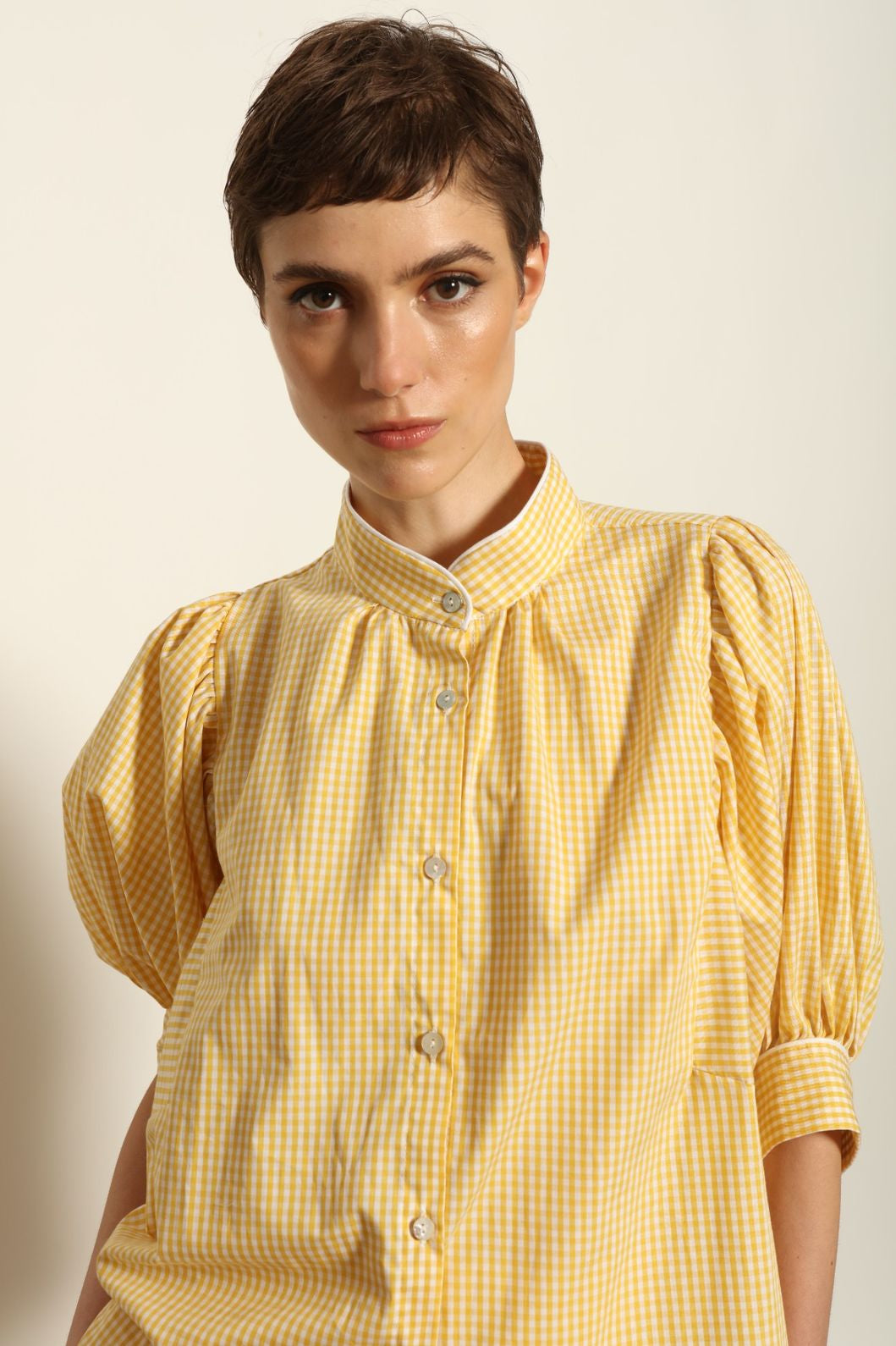 Model wearing the Lola Vichy Butter Yellow Blouse by House of Woven Stories, featuring 100% organic cotton fabric, butter yellow gingham check, short balloon sleeves, and contrasting white piping details.
