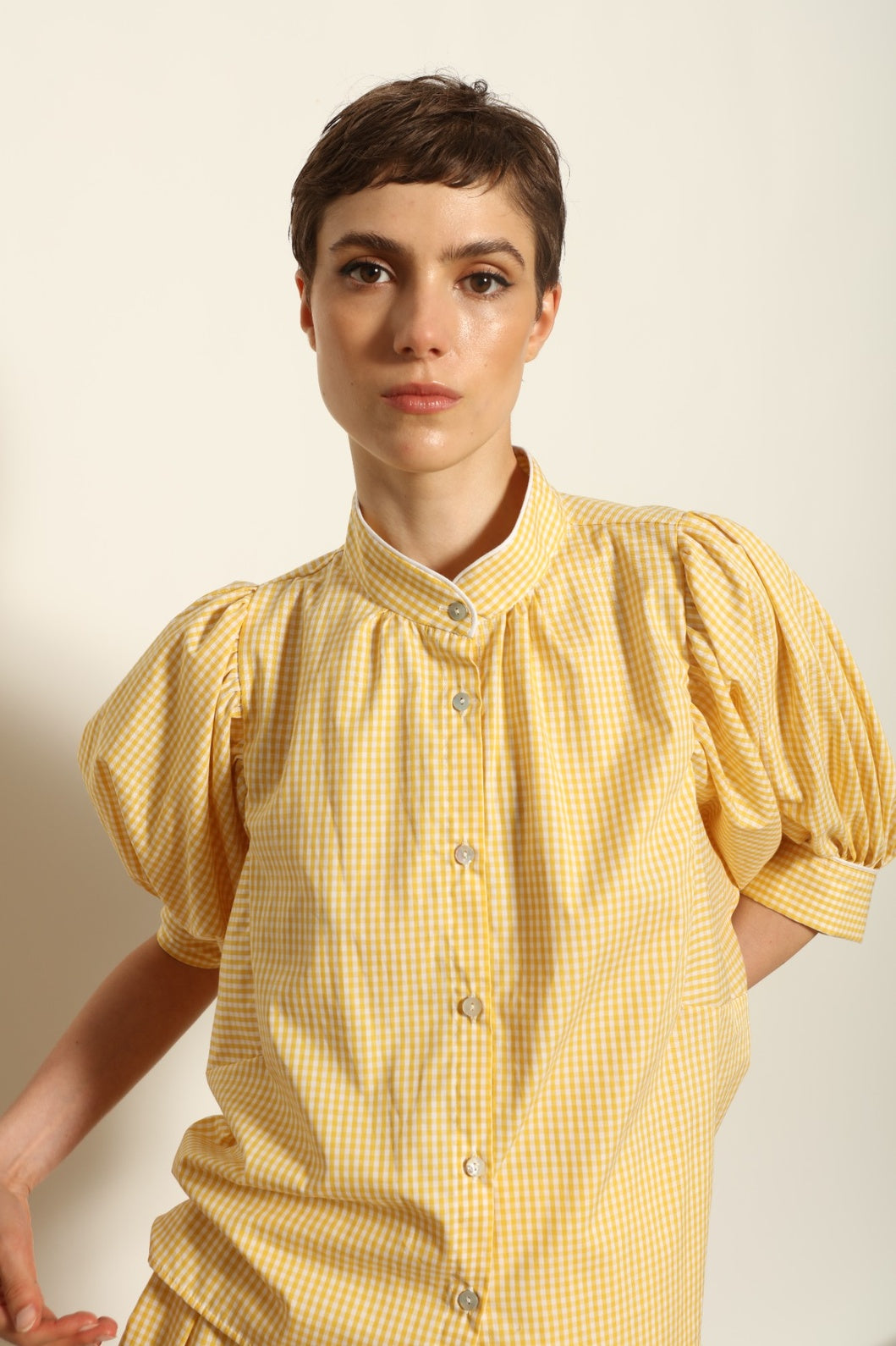 Model wearing the Lola Vichy Butter Yellow Blouse by House of Woven Stories, featuring 100% organic cotton fabric, butter yellow gingham check, short balloon sleeves, and contrasting white piping details.
