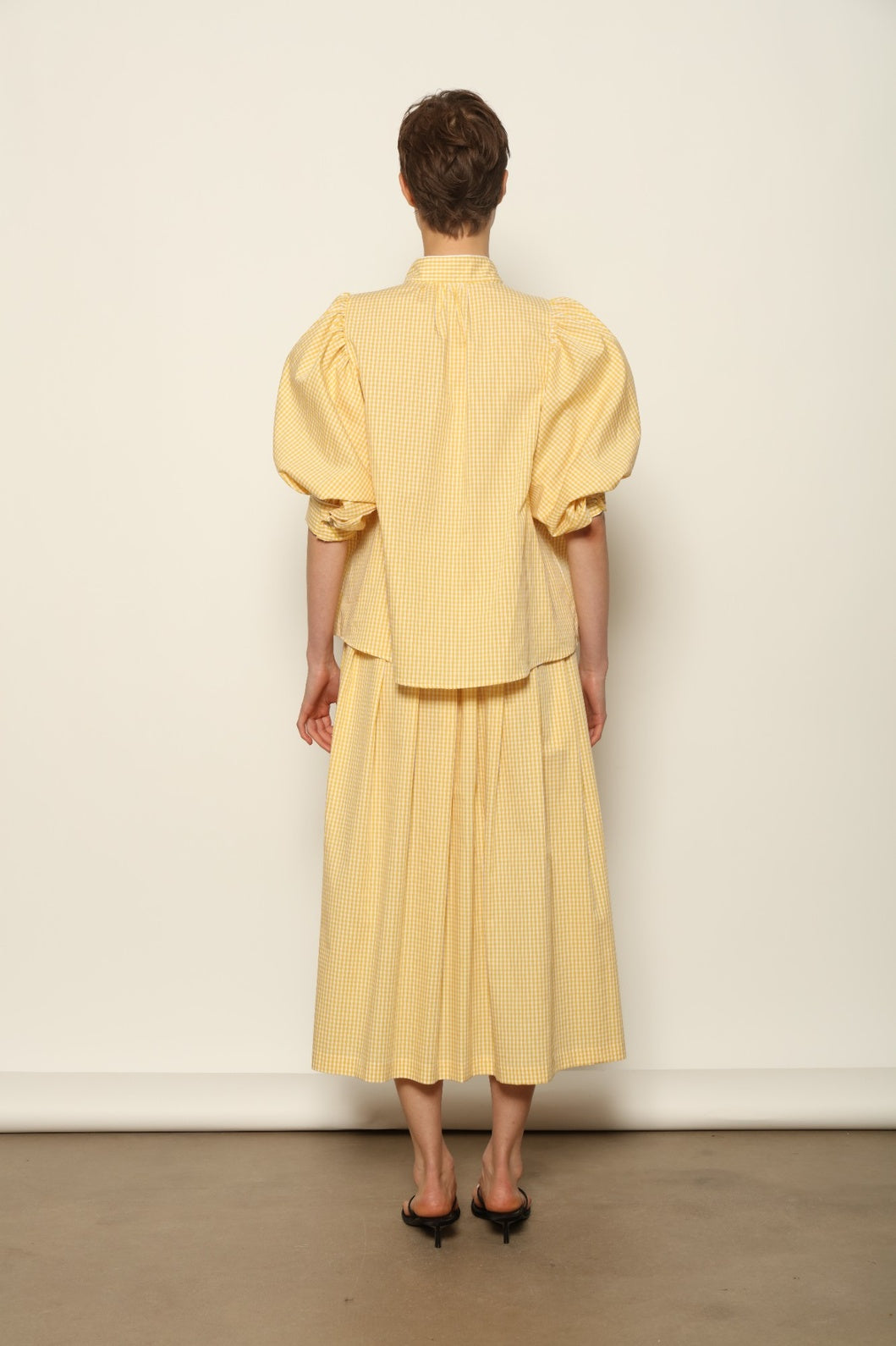 Model wearing the Lola Vichy Butter Yellow Blouse by House of Woven Stories, featuring 100% organic cotton fabric, butter yellow gingham check, short balloon sleeves, and contrasting white piping details.