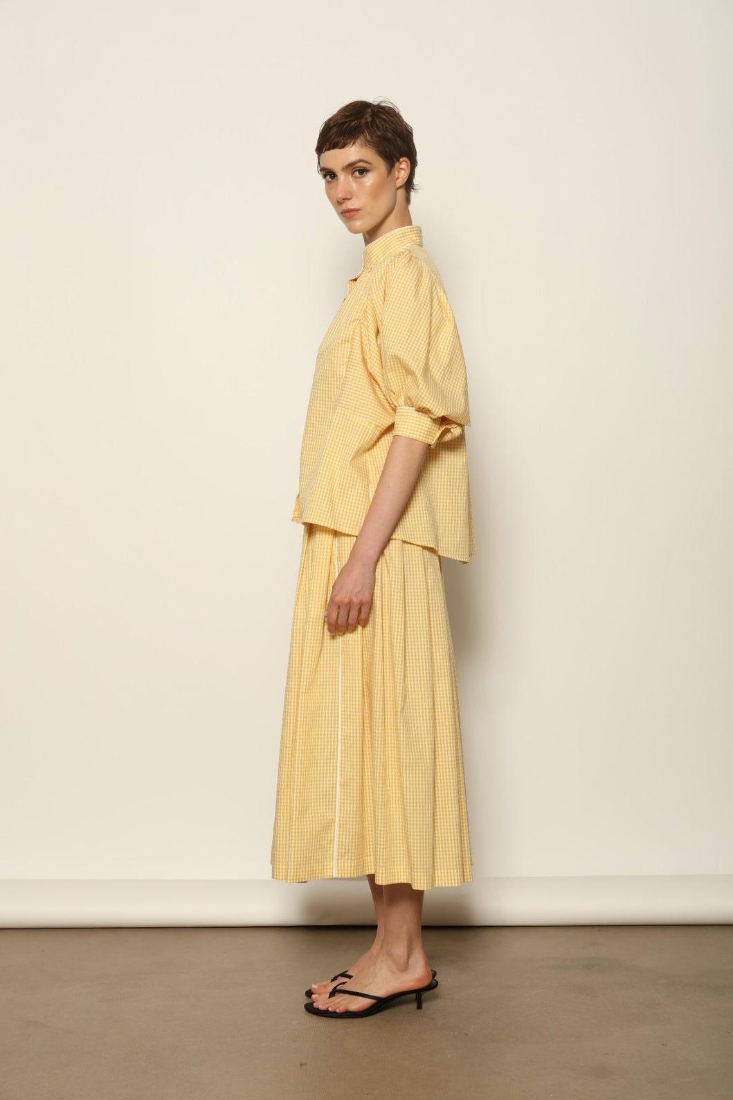 Model wearing the Lola Vichy Butter Yellow Blouse by House of Woven Stories, featuring 100% organic cotton fabric, butter yellow gingham check, short balloon sleeves, and contrasting white piping details.