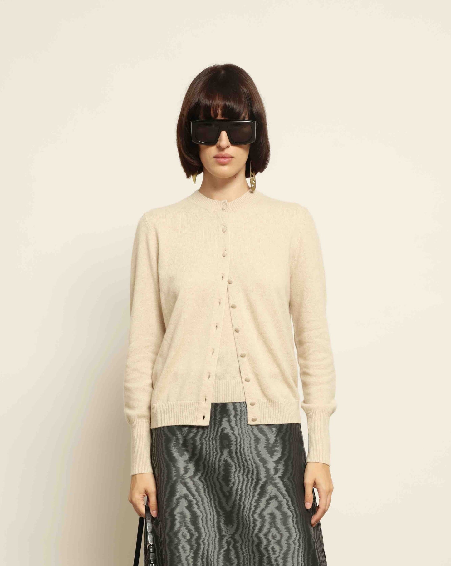 Model is wearing House of Woven Stories Nathalie Coreana Cardigan in natural undyed pure cashmere, long sleeves, round neckline, buttoned front, handmade in Italy with ultra-fine fibers from Inner Mongolia and Tibet.