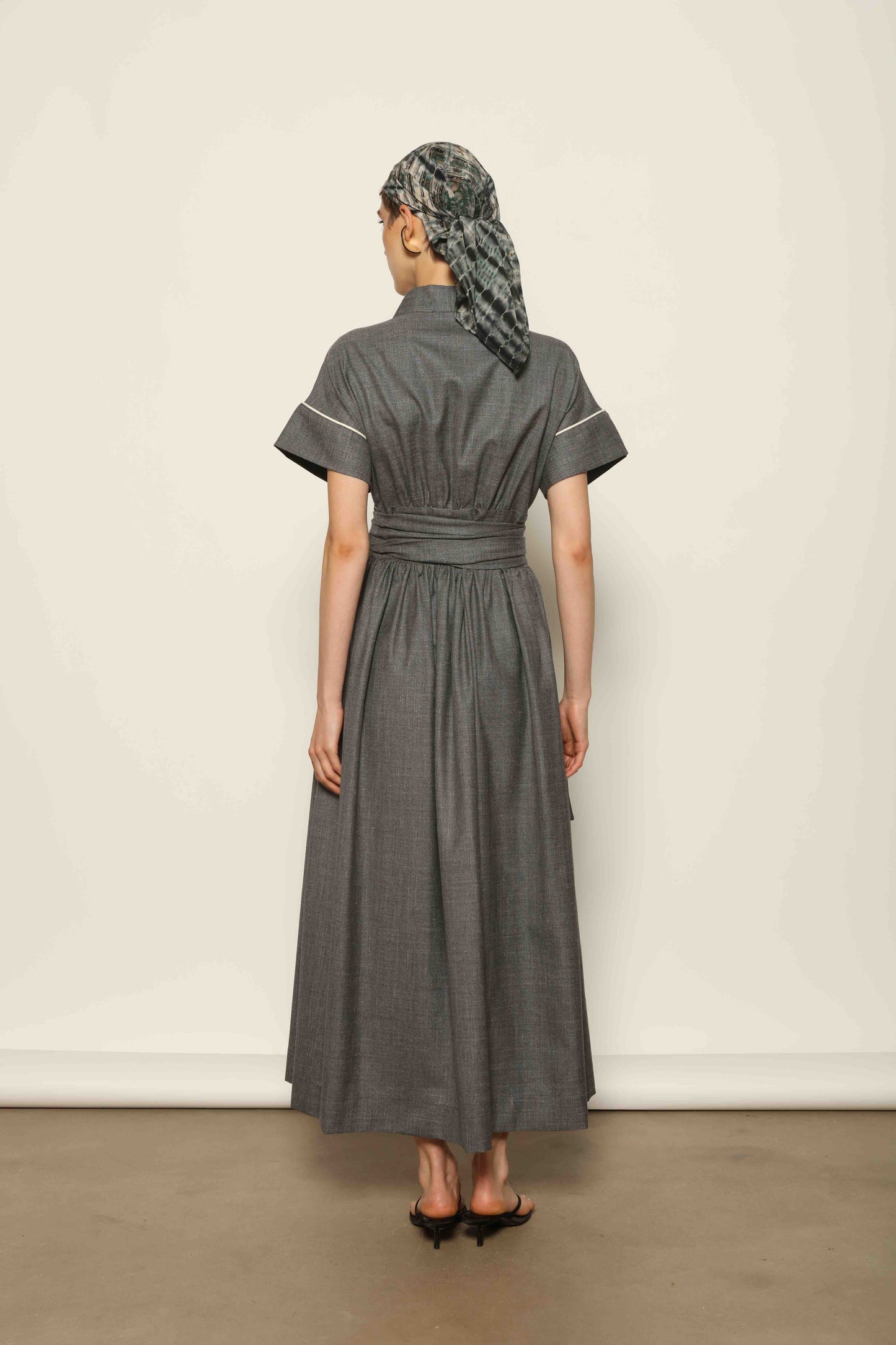 Model wearing the Saint Remy Grey Off White Midi Dress by House of Woven Stories, featuring a wrap silhouette, adjustable belt, half sleeves, and subtle white piping detail in a fluid elegant fabric.