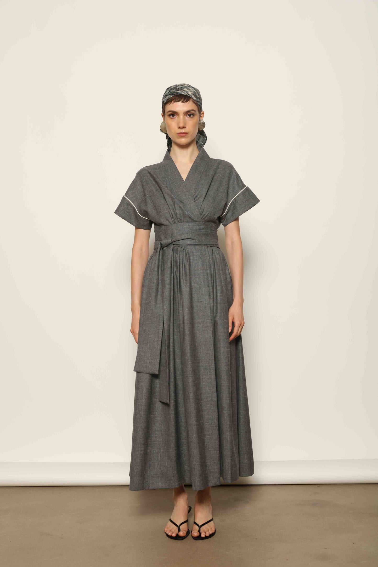 Model wearing the Saint Remy Grey Off White Midi Dress by House of Woven Stories, featuring a wrap silhouette, adjustable belt, half sleeves, and subtle white piping detail in a fluid elegant fabric.