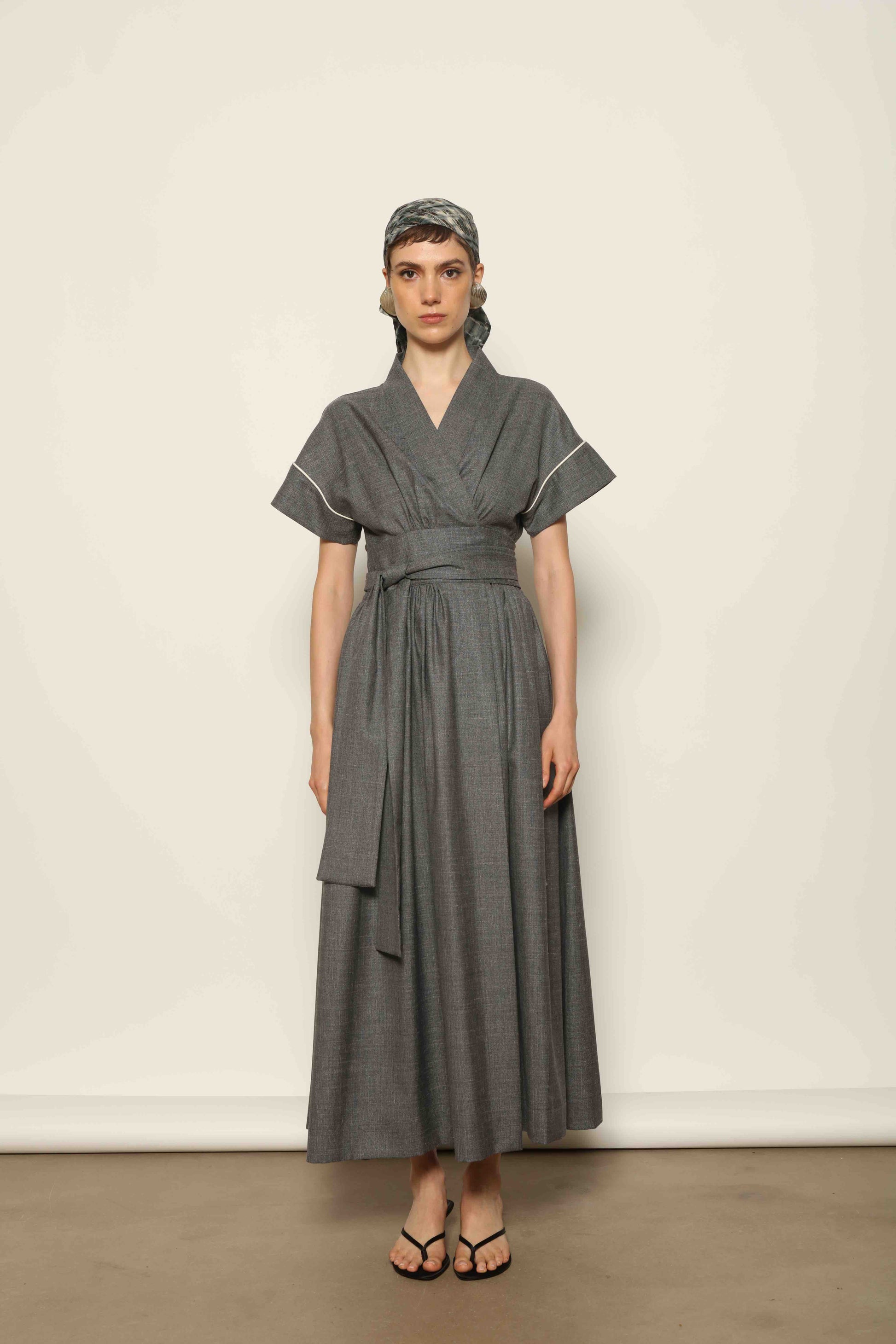 Model wearing the Saint Remy Grey Off White Midi Dress by House of Woven Stories, featuring a wrap silhouette, adjustable belt, half sleeves, and subtle white piping detail in a fluid elegant fabric.