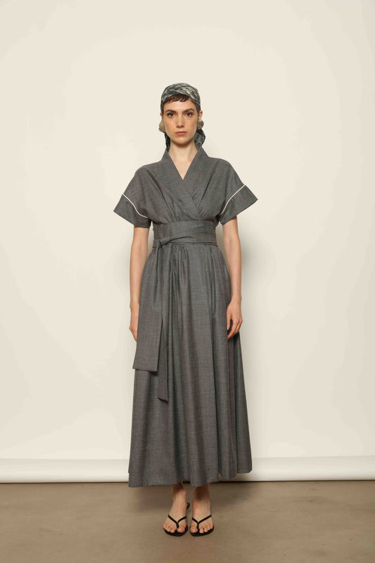 Model wearing the Saint Remy Grey Off White Midi Dress by House of Woven Stories, featuring a wrap silhouette, adjustable belt, half sleeves, and subtle white piping detail in a fluid elegant fabric.
