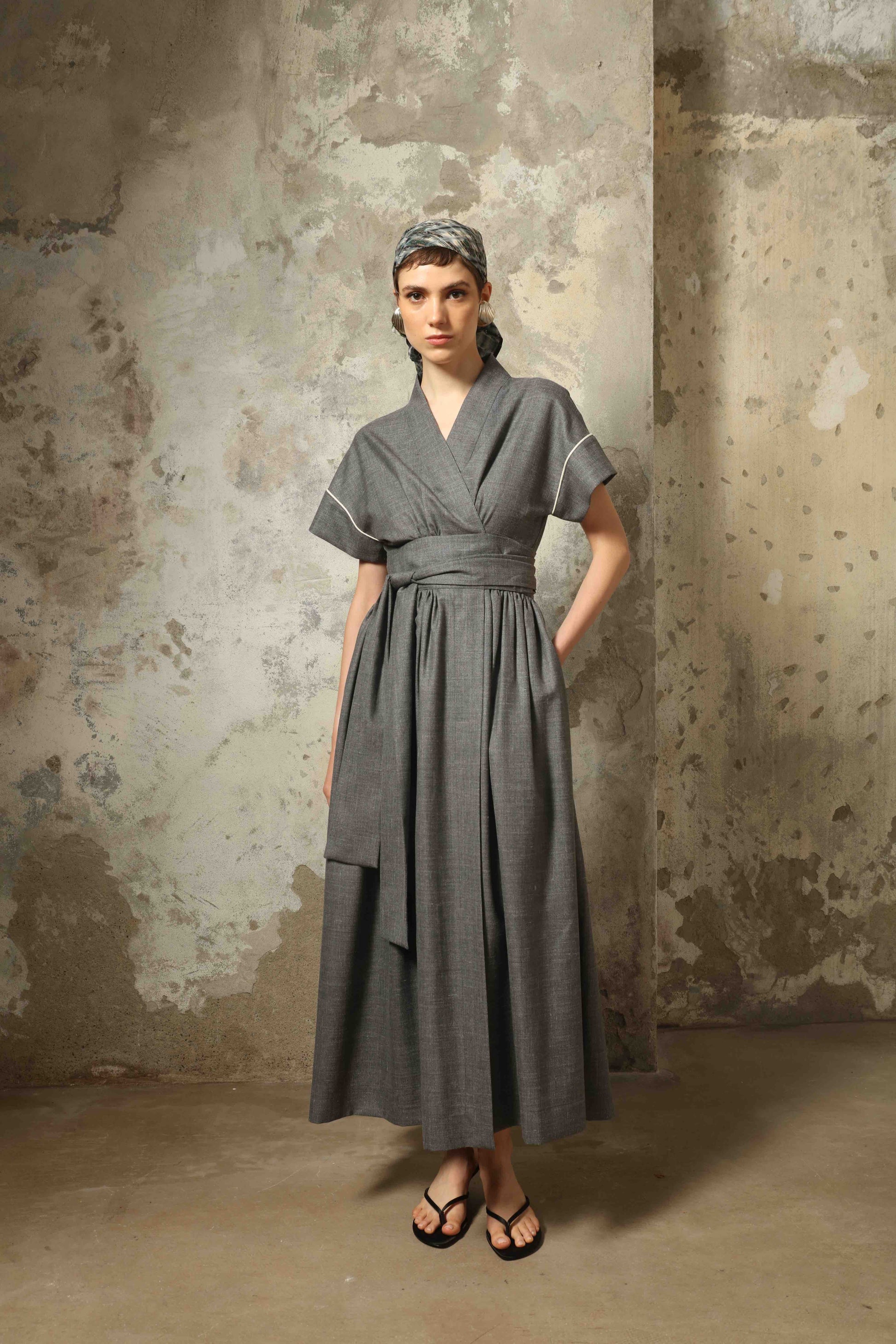 Model wearing the Saint Remy Grey Off White Midi Dress by House of Woven Stories, featuring a wrap silhouette, adjustable belt, half sleeves, and subtle white piping detail in a fluid elegant fabric.