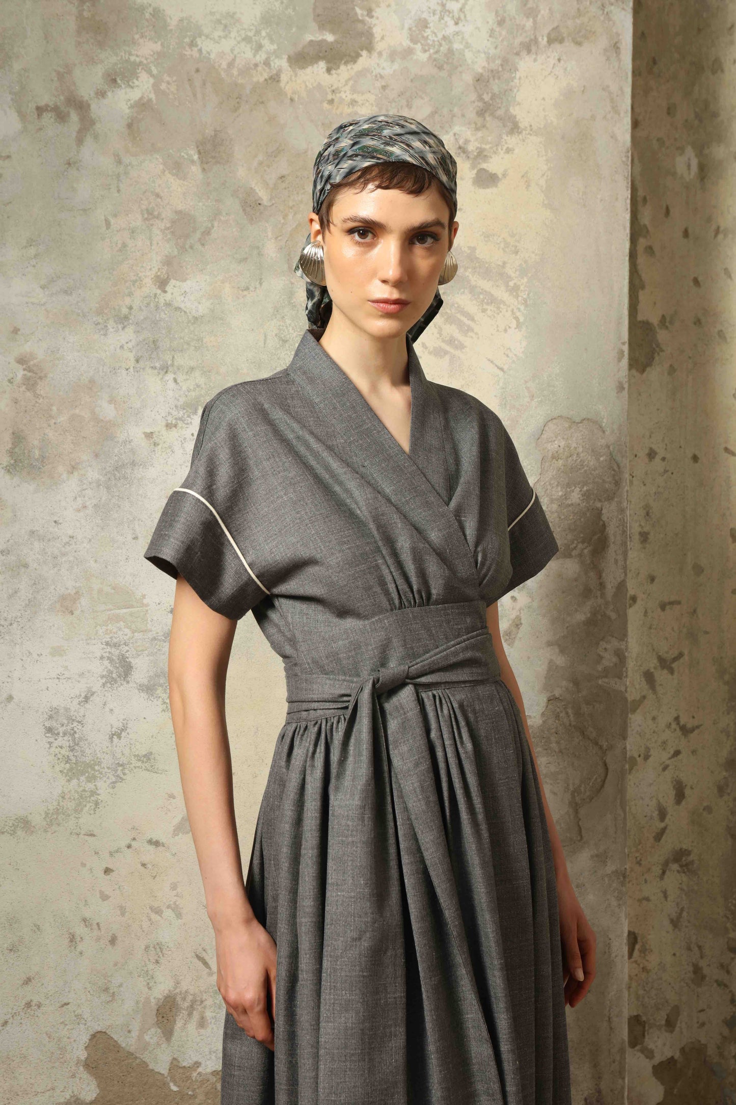 Model wearing the Saint Remy Grey Off White Midi Dress by House of Woven Stories, featuring a wrap silhouette, adjustable belt, half sleeves, and subtle white piping detail in a fluid elegant fabric.