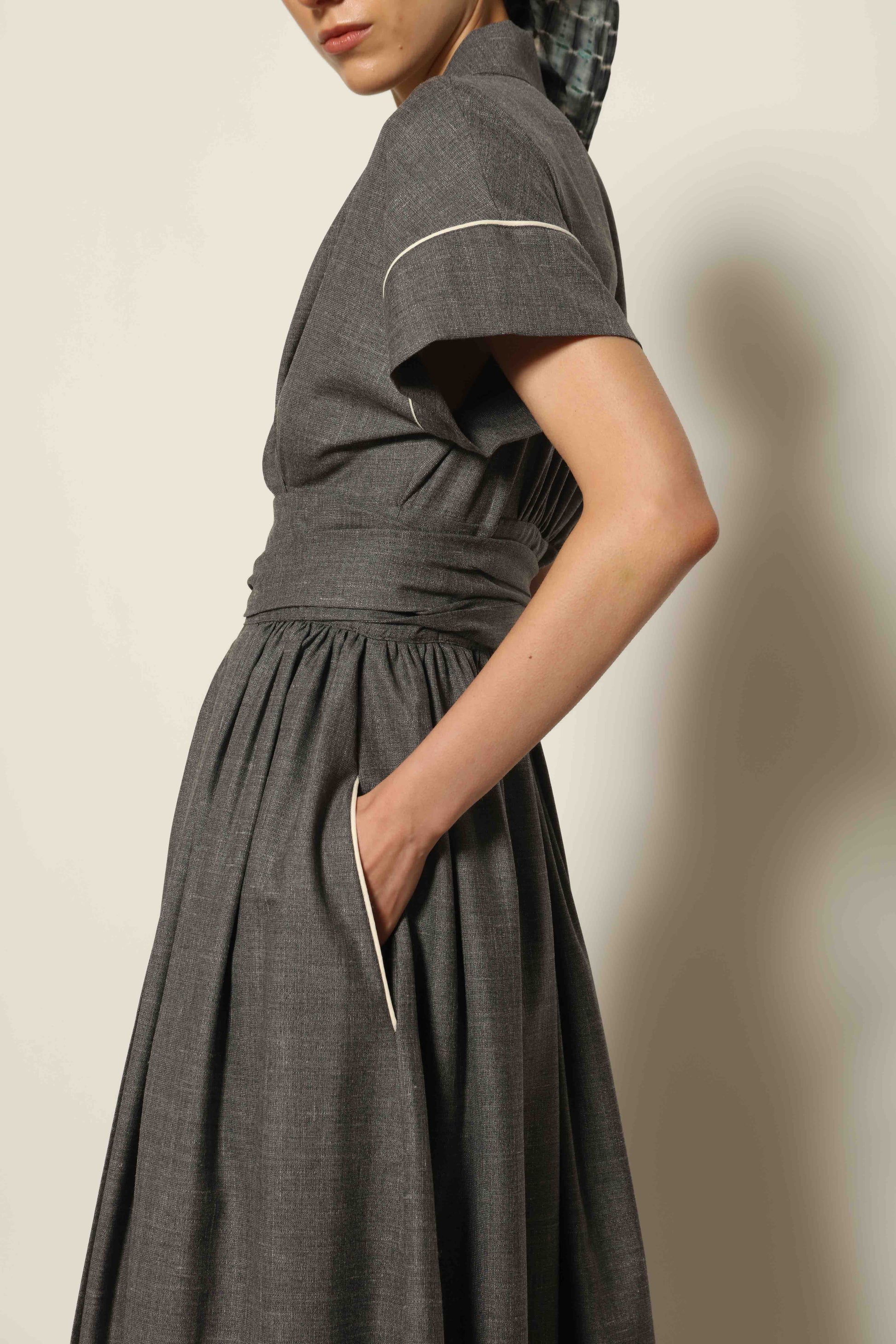 Model wearing the Saint Remy Grey Off White Midi Dress by House of Woven Stories, featuring a wrap silhouette, adjustable belt, half sleeves, and subtle white piping detail in a fluid elegant fabric.