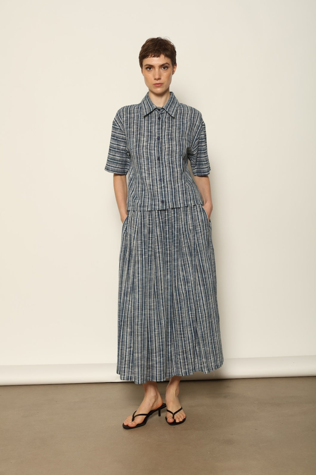 Model wearing the Seoul Indigo Blue Striped Ikat Midi Skirt by House of Woven Stories, crafted from handwoven Kala cotton with an indigo blue and off-white ikat pattern, elasticated waistband, and relaxed midi silhouette.