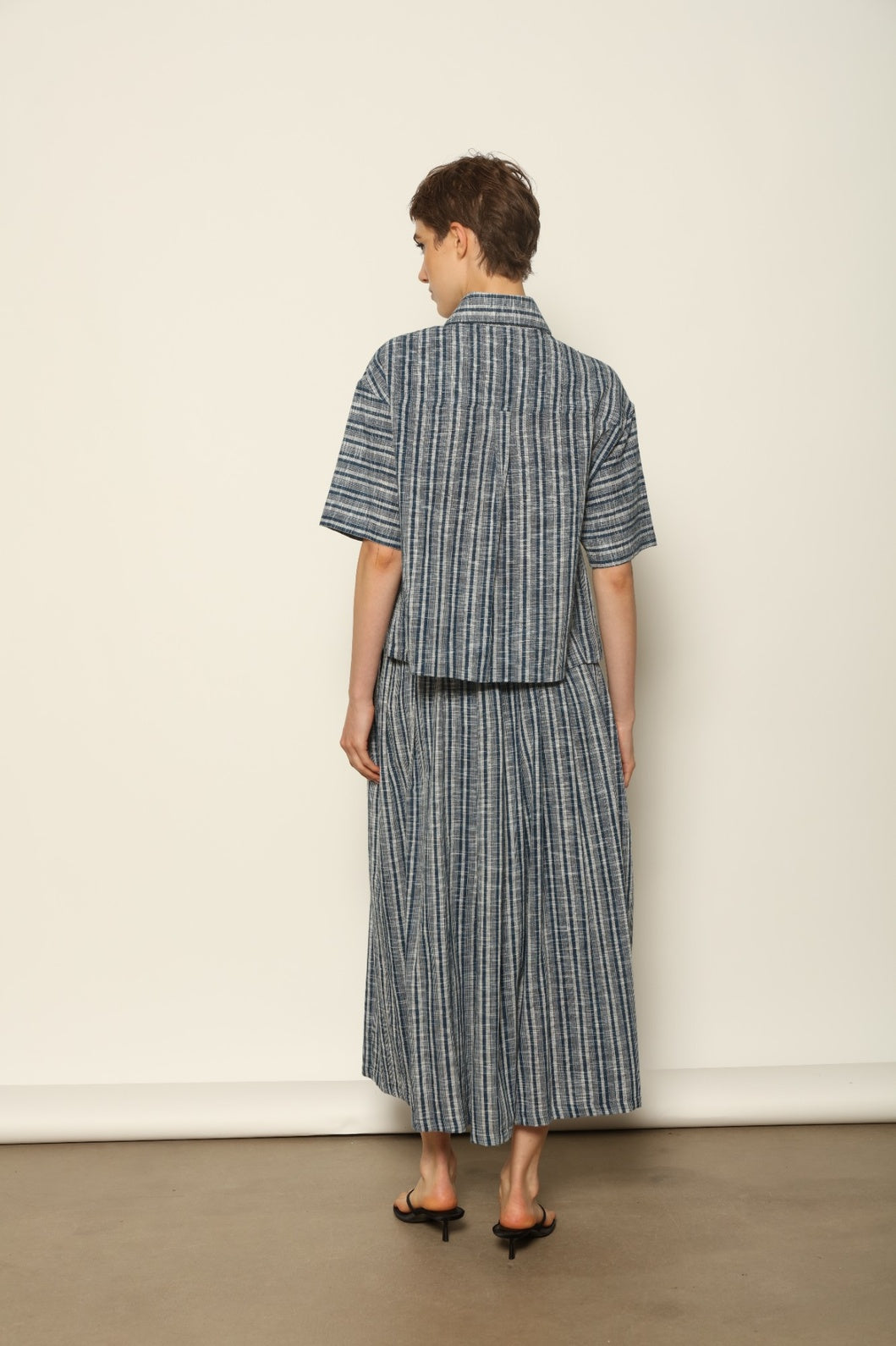Model wearing the Seoul Indigo Blue Striped Ikat Midi Skirt by House of Woven Stories, crafted from handwoven Kala cotton with an indigo blue and off-white ikat pattern, elasticated waistband, and relaxed midi silhouette.