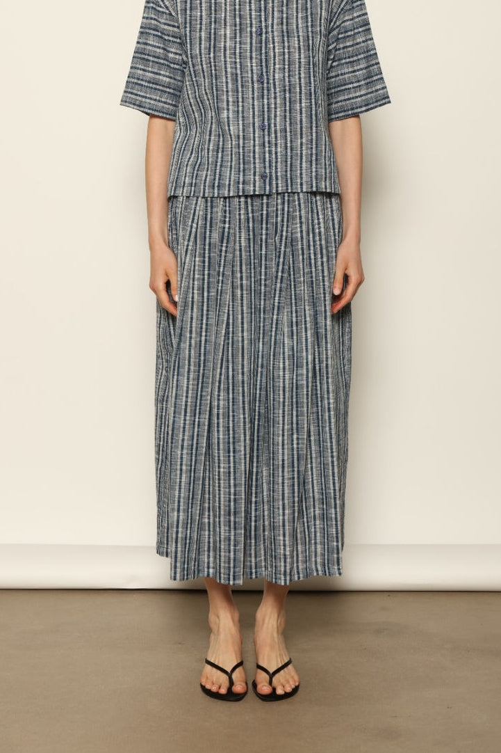 Model wearing the Seoul Indigo Blue Striped Ikat Midi Skirt by House of Woven Stories, crafted from handwoven Kala cotton with an indigo blue and off-white ikat pattern, elasticated waistband, and relaxed midi silhouette.