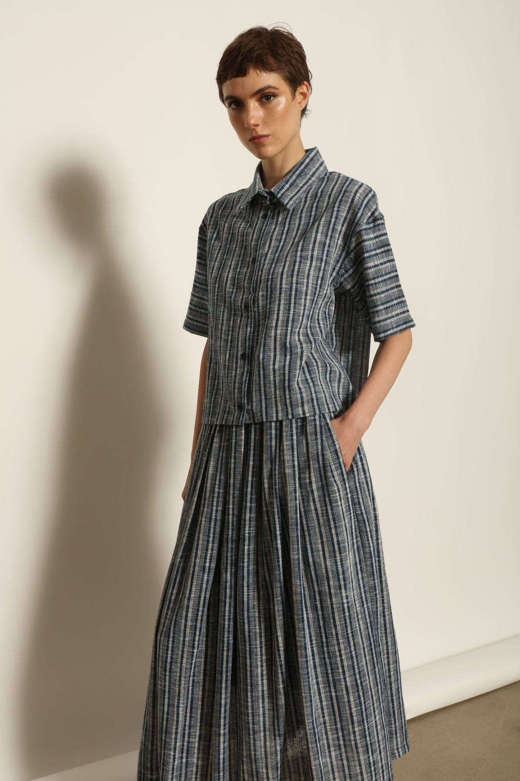 Model wearing the Seoul Indigo Blue Striped Ikat Midi Skirt by House of Woven Stories, crafted from handwoven Kala cotton with an indigo blue and off-white ikat pattern, elasticated waistband, and relaxed midi silhouette.