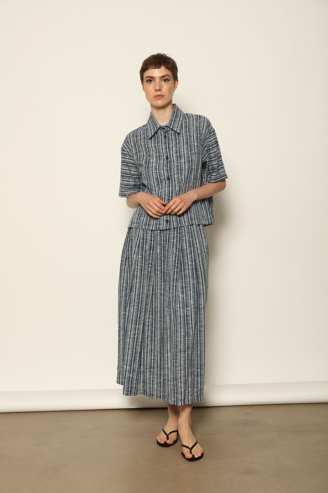 Model wearing the Seoul Indigo Blue Striped Ikat Midi Skirt by House of Woven Stories, crafted from handwoven Kala cotton with an indigo blue and off-white ikat pattern, elasticated waistband, and relaxed midi silhouette.