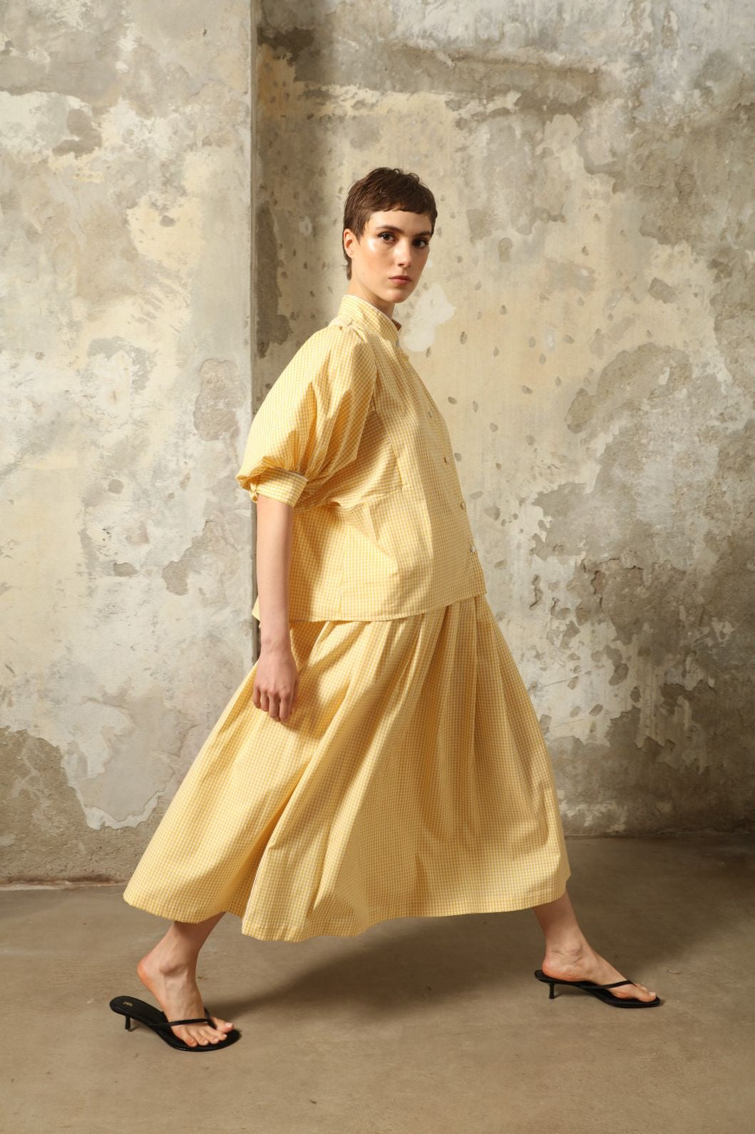 Model wearing the Seoul Vichy Butter Yellow Skirt by House of Woven Stories, featuring a butter yellow gingham pattern, draped silhouette, white piping waistband, and elegant summer design.