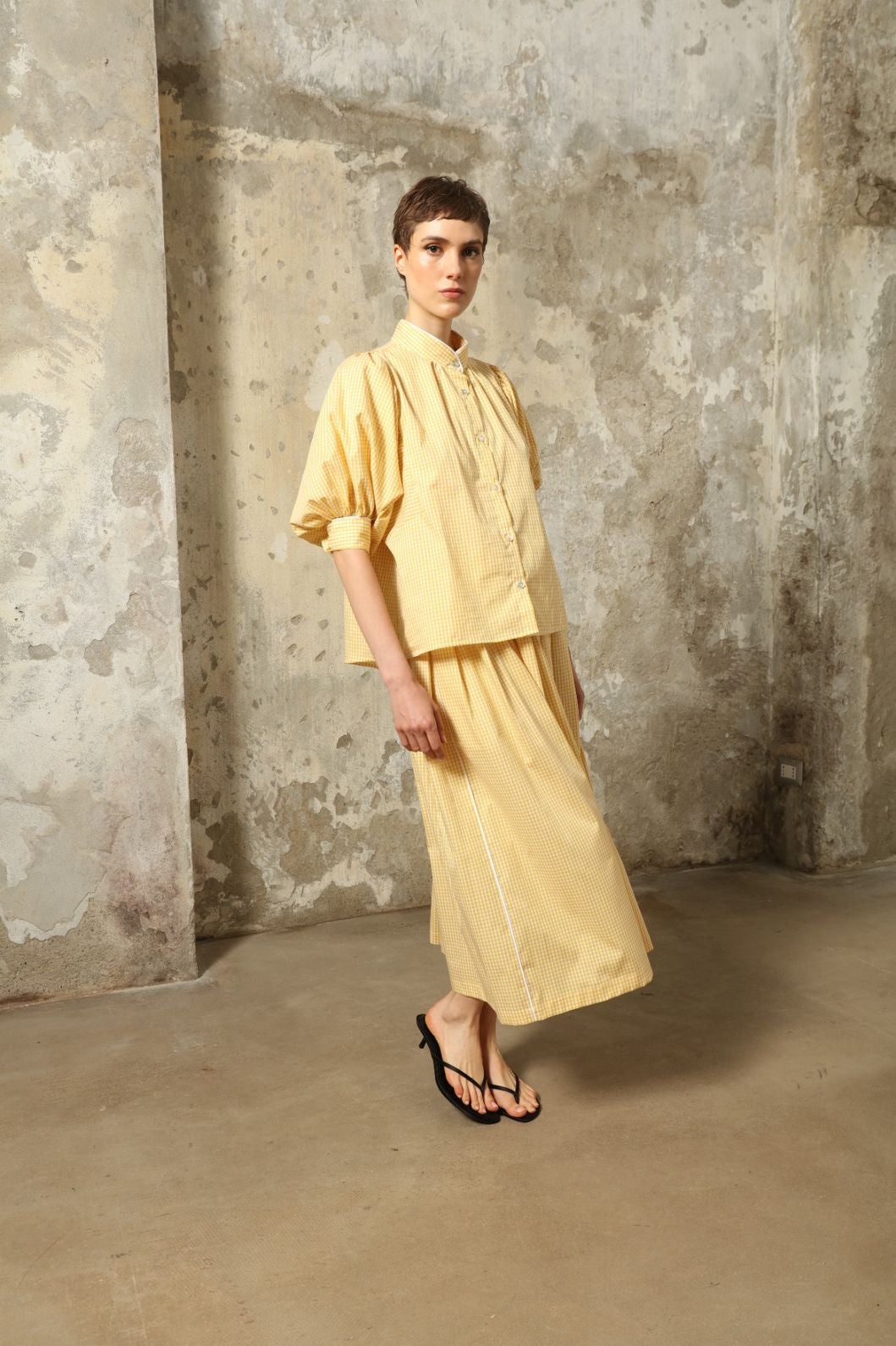 Model wearing the Seoul Vichy Butter Yellow Skirt by House of Woven Stories, featuring a butter yellow gingham pattern, draped silhouette, white piping waistband, and elegant summer design.