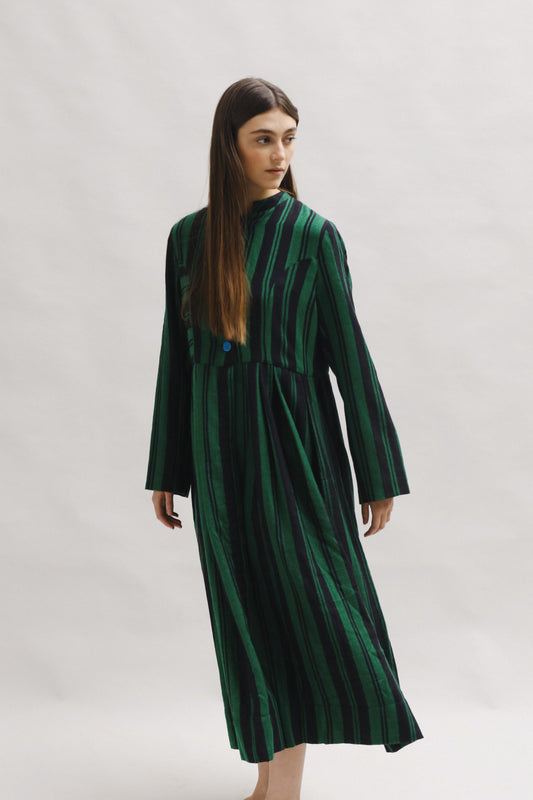 Model is wearing the Folklore 34 silk and wool striped dress by Injiri, featuring bold green and black stripes and sky blue buttons, artisan-made in India.