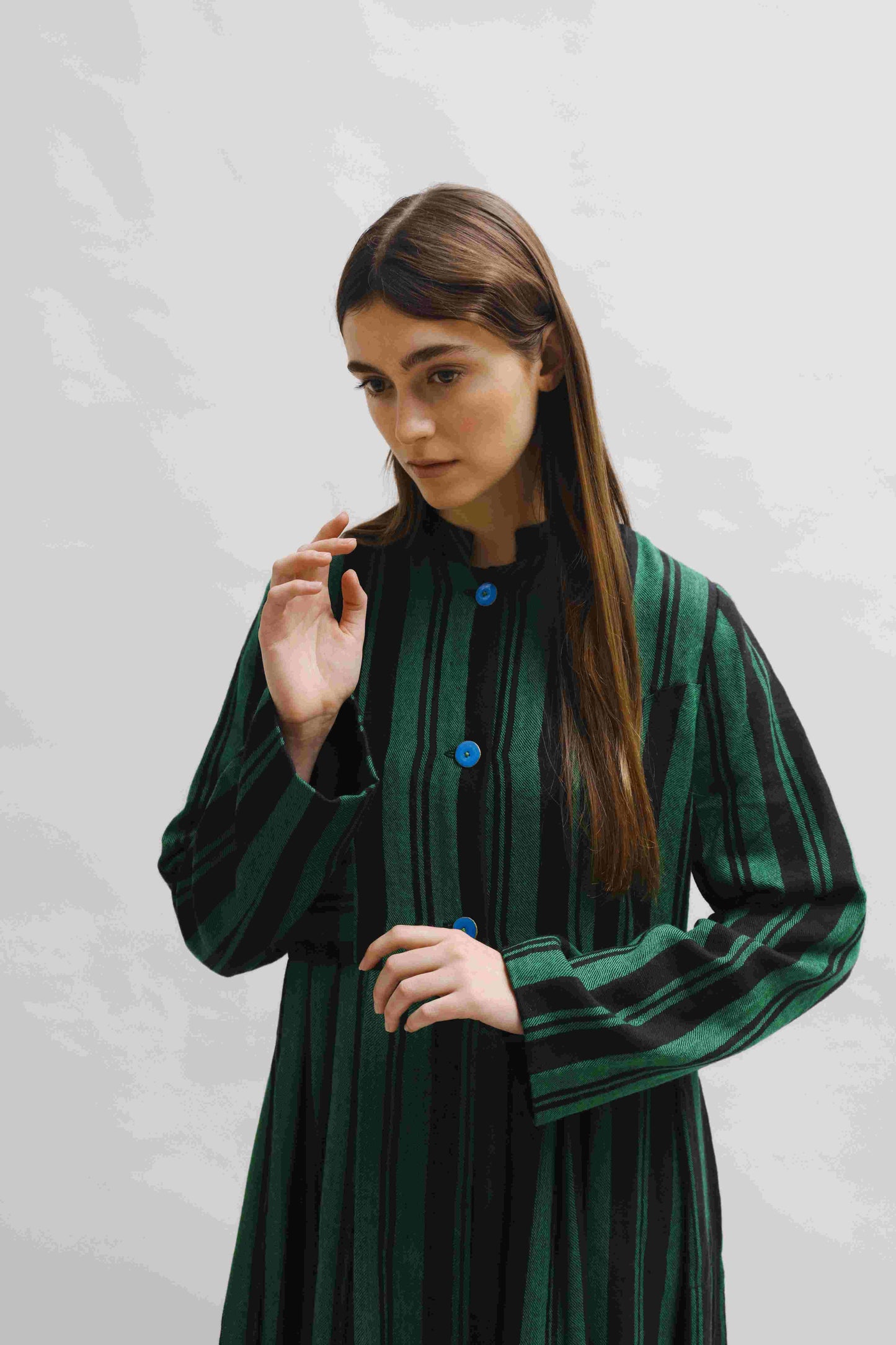 Model is wearing the Folklore 34 silk and wool striped dress by Injiri, featuring bold green and black stripes and sky blue buttons, artisan-made in India.
