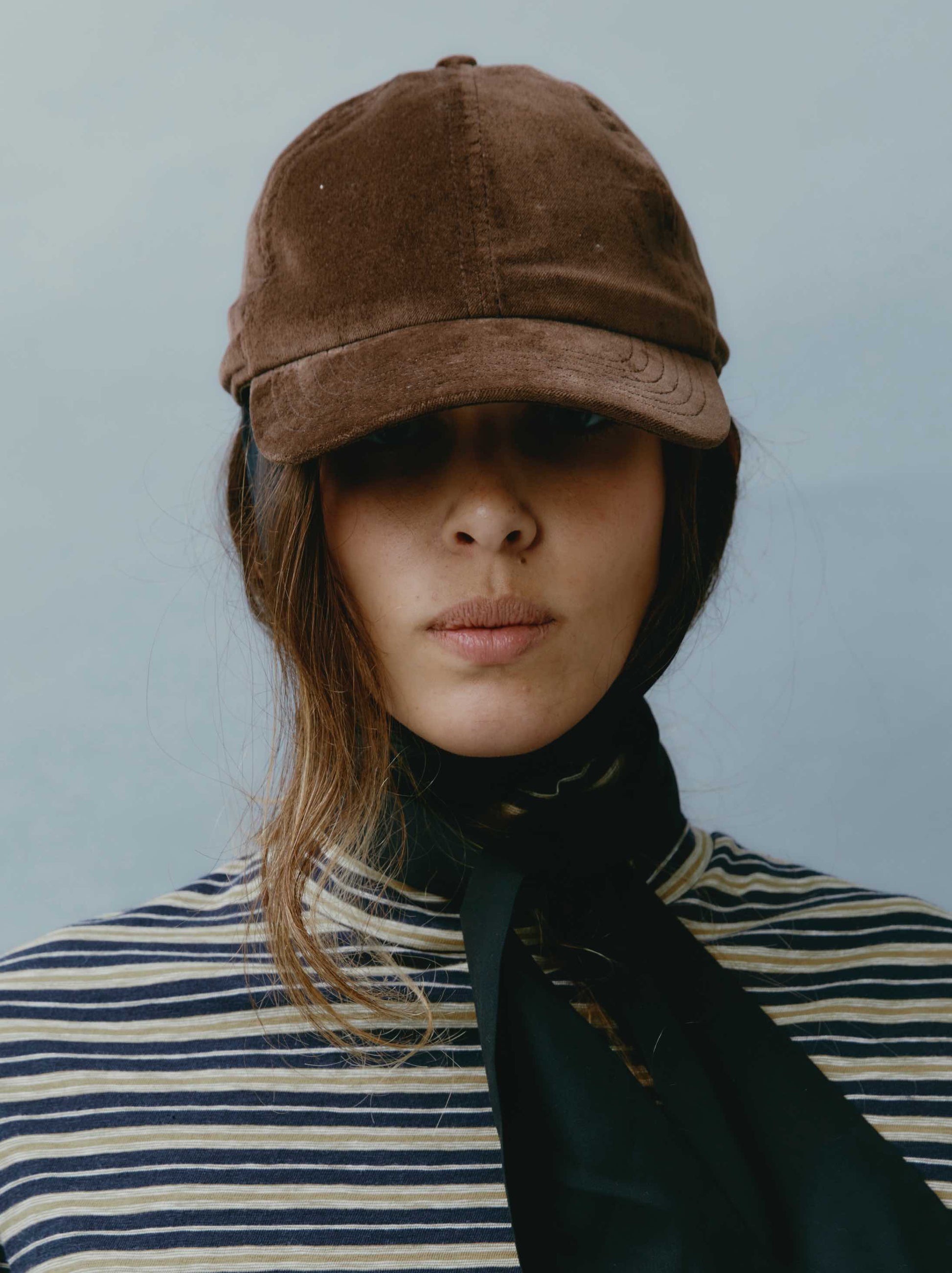 Model is wearing the Kate Velvet Cap by Maison Jejia, part of the House of Woven Stories selection, featuring soft cotton velvet, warm brown color, structured shape, and adjustable closure.
