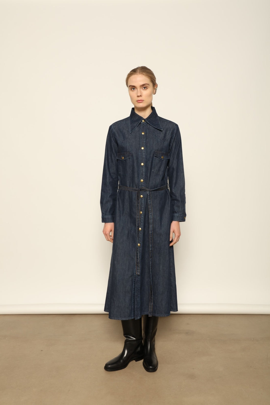 Model is wearing La Robe Star in Bleu D’été by Happy Haus, a denim shirt dress with relaxed fit, chest pockets, matching belt, and golden button detail, combining timeless style with versatile year-round wear.