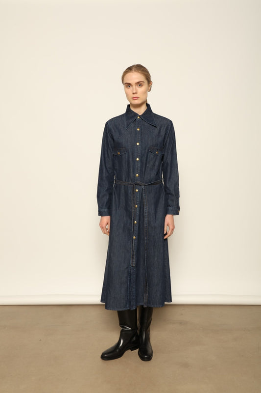 Model is wearing La Robe Star in Bleu D’été by Happy Haus, a denim shirt dress with relaxed fit, chest pockets, matching belt, and golden button detail, combining timeless style with versatile year-round wear.