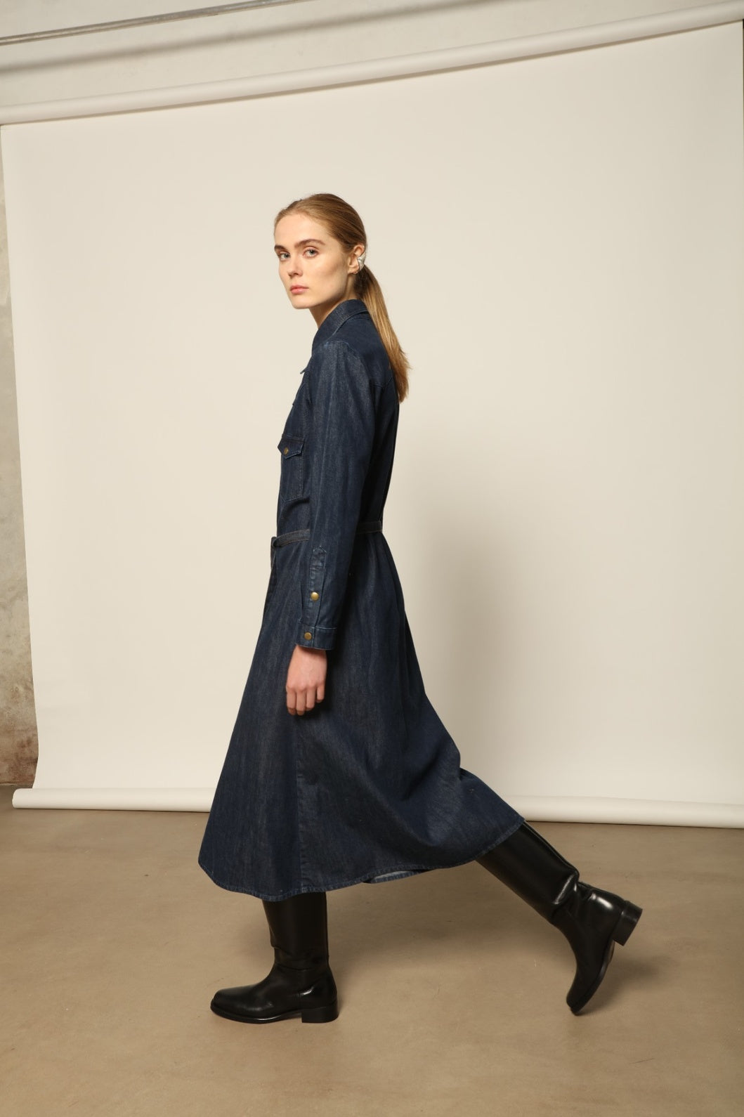 Model is wearing La Robe Star in Bleu D’été by Happy Haus, a denim shirt dress with relaxed fit, chest pockets, matching belt, and golden button detail, combining timeless style with versatile year-round wear.