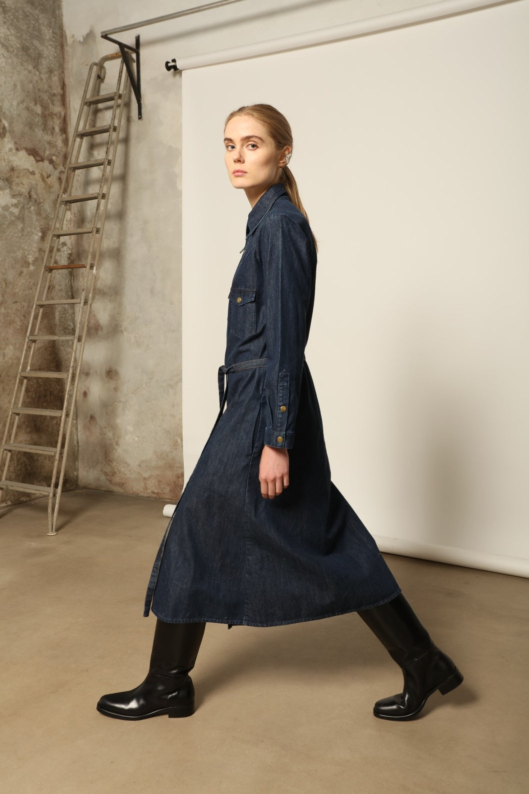 Model is wearing La Robe Star in Bleu D’été by Happy Haus, a denim shirt dress with relaxed fit, chest pockets, matching belt, and golden button detail, combining timeless style with versatile year-round wear.