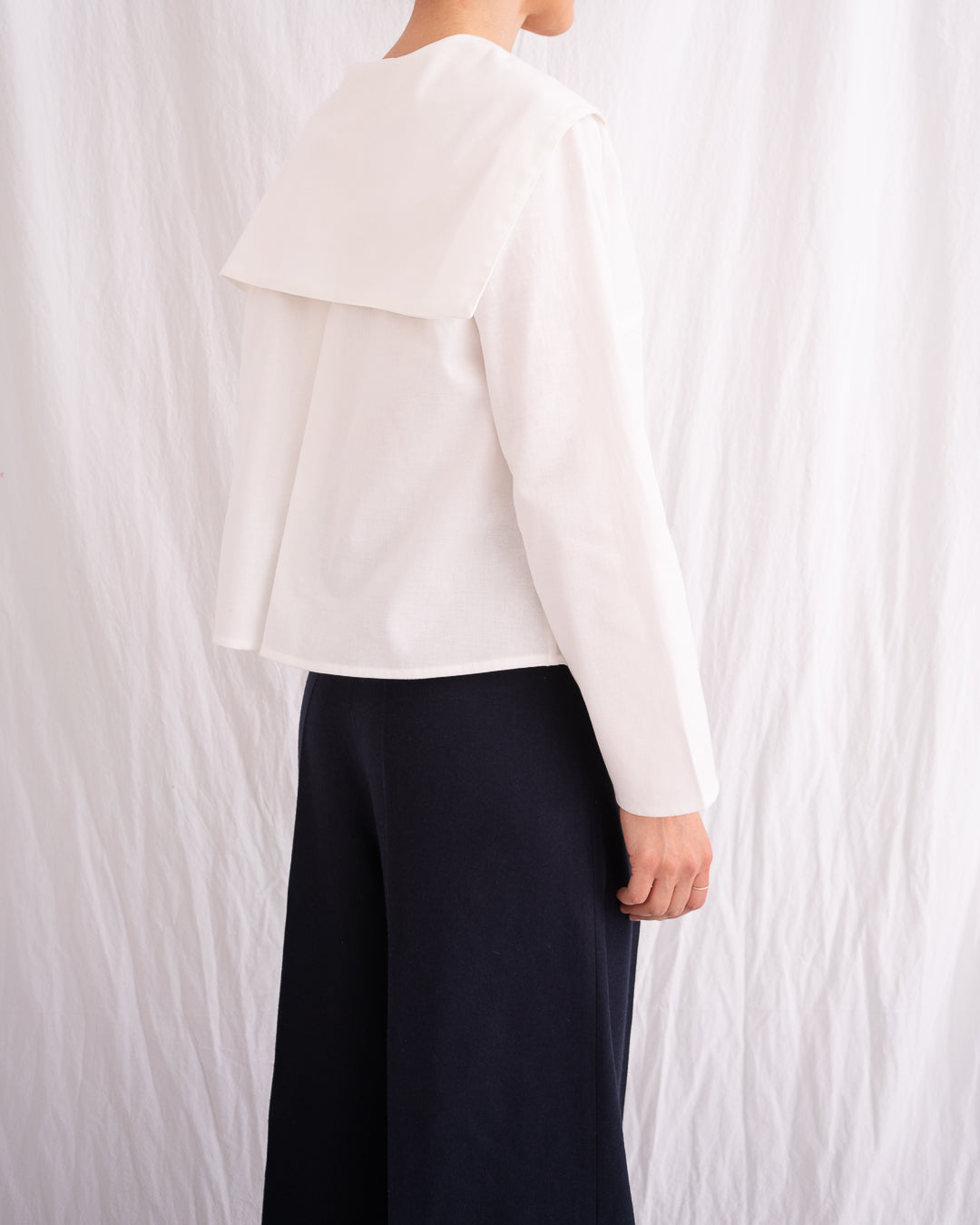 Model is wearing the Le Matelot White Blouse by Les Vacances d’Irina, a long-sleeved cotton blouse with sailor collar, handmade in Romania with artisanal detailing.
