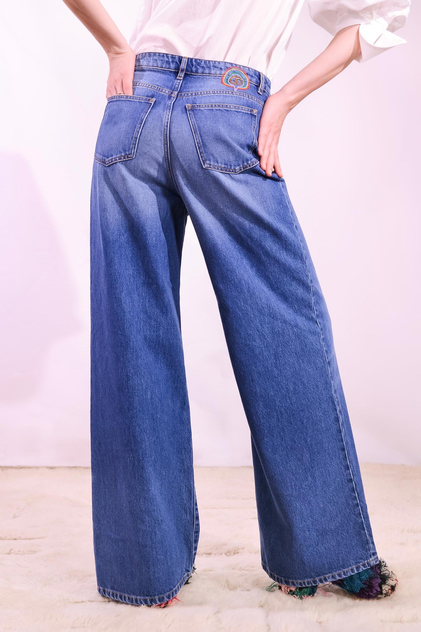 Model is wearing the Le Pantalon Baggy in Bleu d’Été Vintage by Happy Haus - relaxed boyfriend-style recycled denim jeans with wooden button, flower-shaped back pockets, and tobacco-colored topstitching.