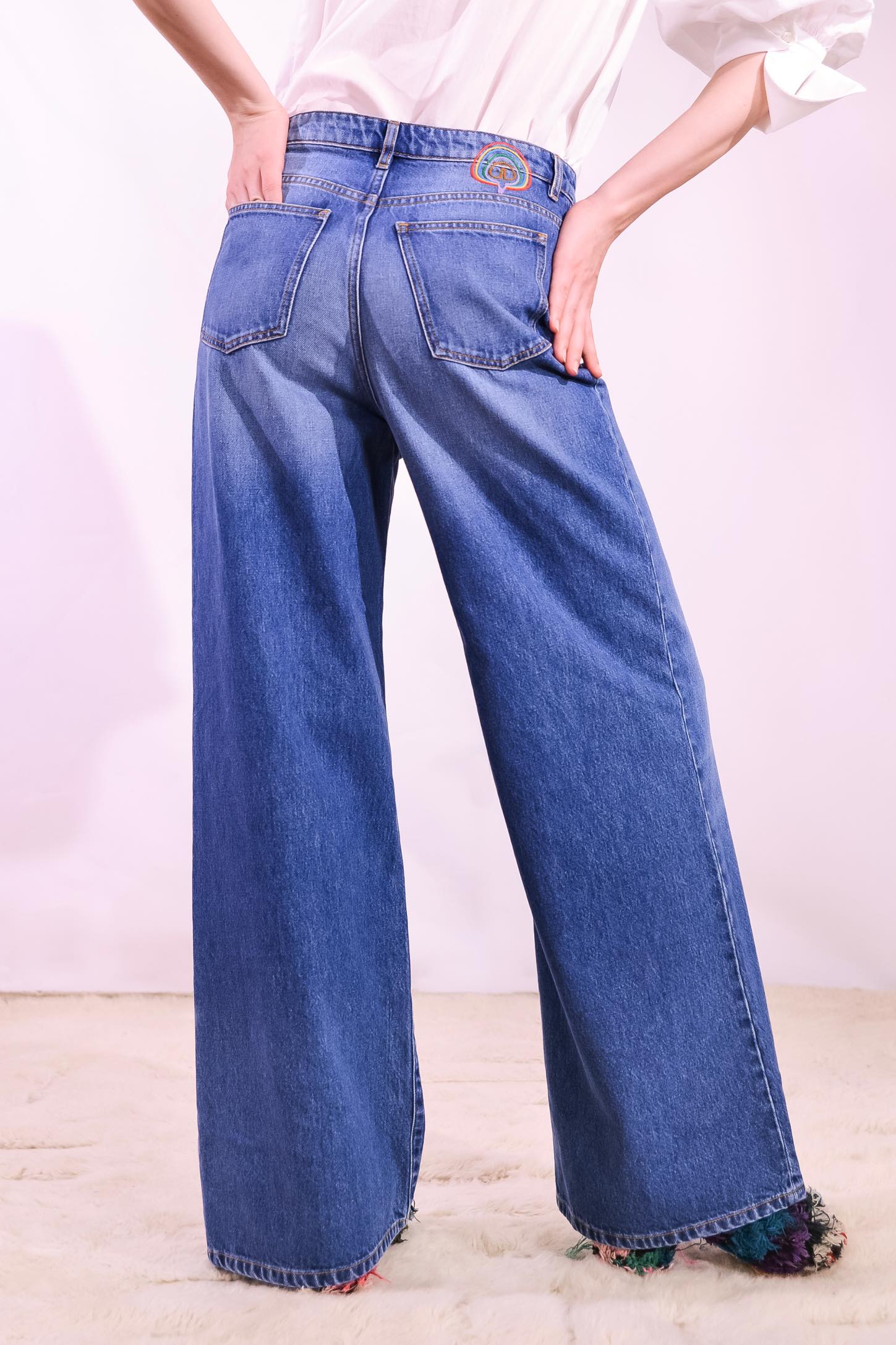 Model is wearing the Le Pantalon Baggy in Bleu d’Été Vintage by Happy Haus - relaxed boyfriend-style recycled denim jeans with wooden button, flower-shaped back pockets, and tobacco-colored topstitching.