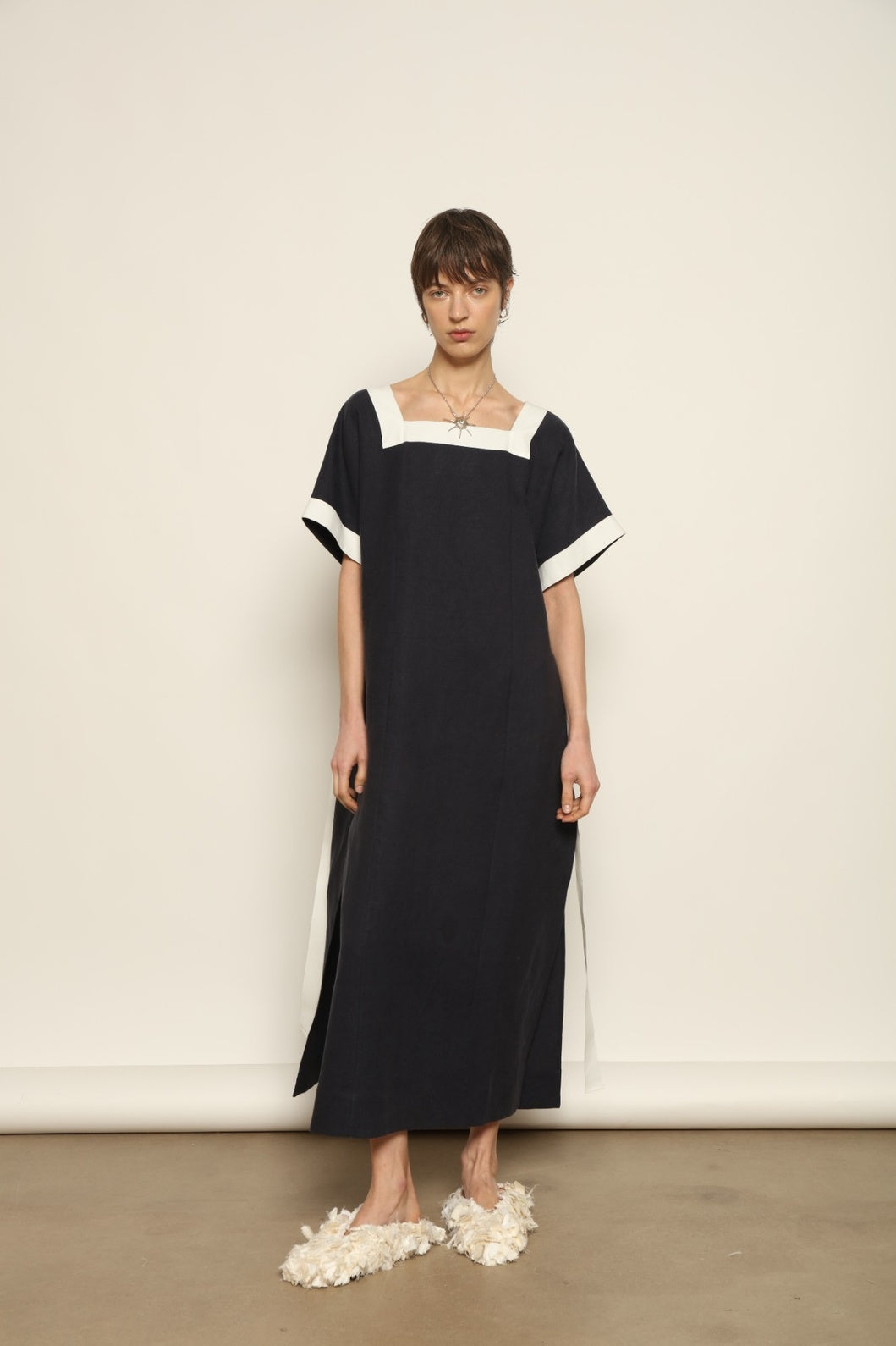 Model is wearing the Les Vacances d’Irina Astypalea kaftan linen dress in white with navy ribbon appliqués, handcrafted in Bucharest, from the House of Nomad Stories selection.