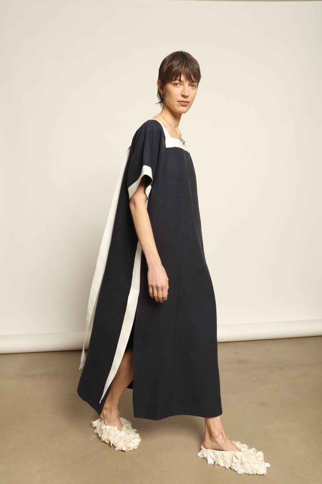 Model is wearing the Les Vacances d’Irina Astypalea kaftan linen dress in white with navy ribbon appliqués, handcrafted in Bucharest, from the House of Nomad Stories selection.