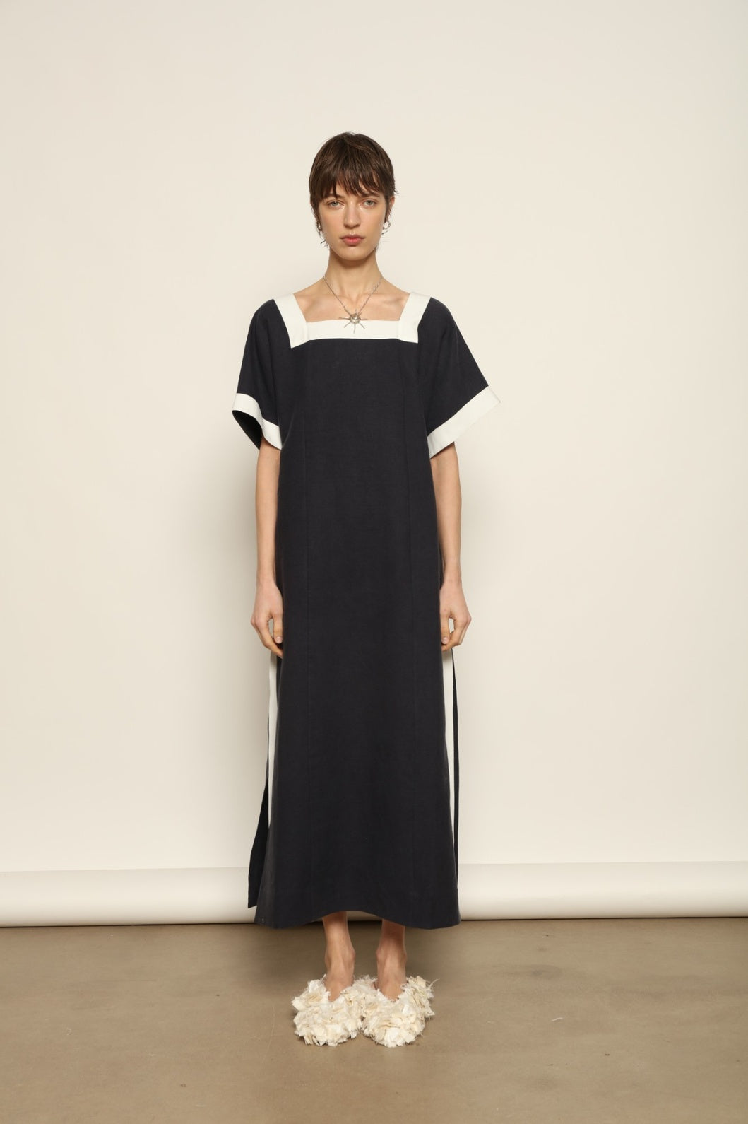 Model is wearing the Les Vacances d’Irina Astypalea kaftan linen dress in white with navy ribbon appliqués, handcrafted in Bucharest, from the House of Nomad Stories selection.