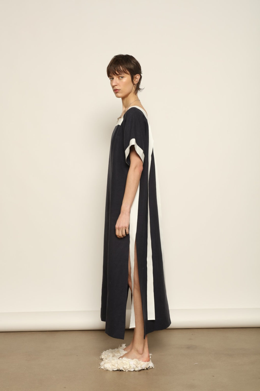 Model is wearing the Les Vacances d’Irina Astypalea kaftan linen dress in white with navy ribbon appliqués, handcrafted in Bucharest, from the House of Nomad Stories selection.