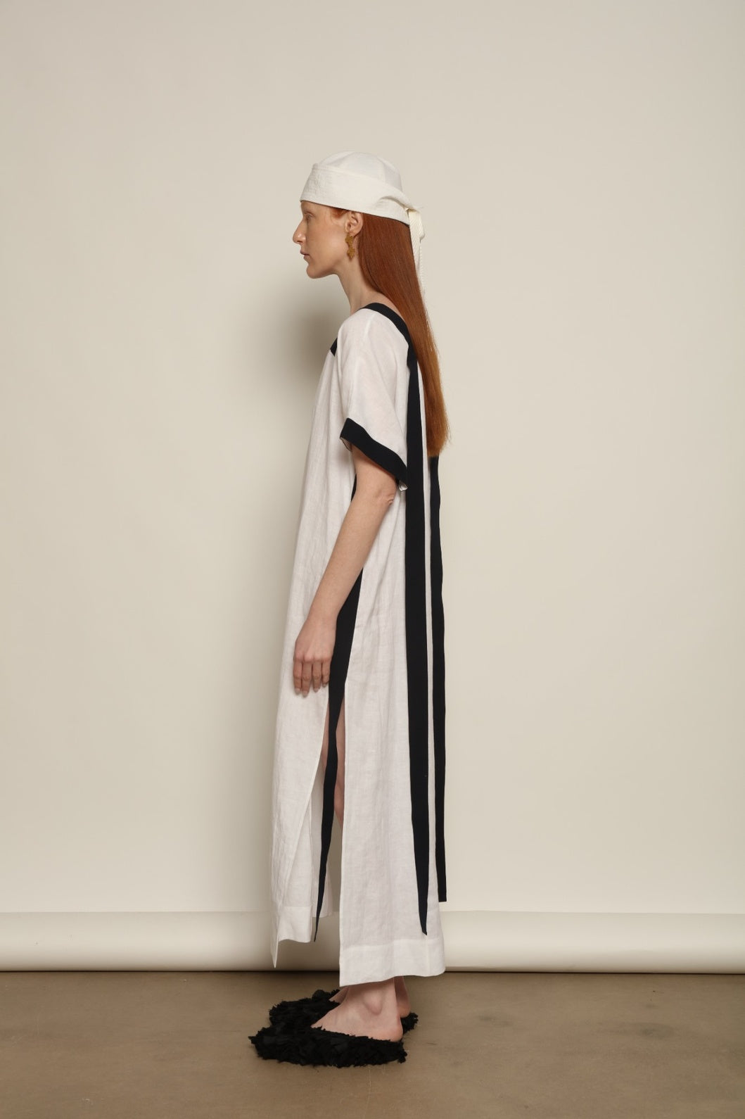 Model is wearing the Les Vacances d’Irina Astypalea kaftan linen dress in white with navy ribbon appliqués, handcrafted in Bucharest, from the House of Nomad Stories selection.