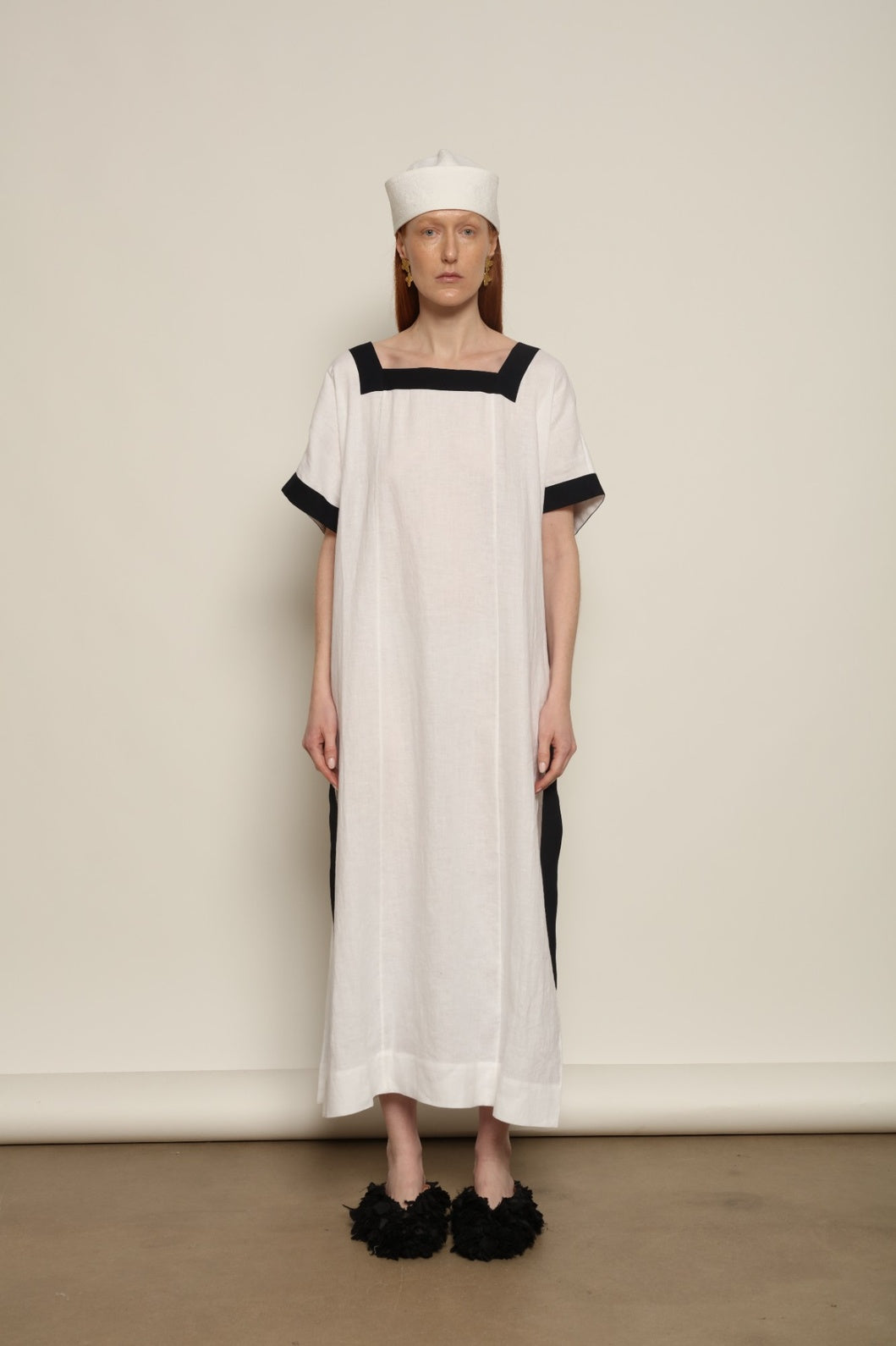 Model is wearing the Les Vacances d’Irina Astypalea kaftan linen dress in white with navy ribbon appliqués, handcrafted in Bucharest, from the House of Nomad Stories selection.