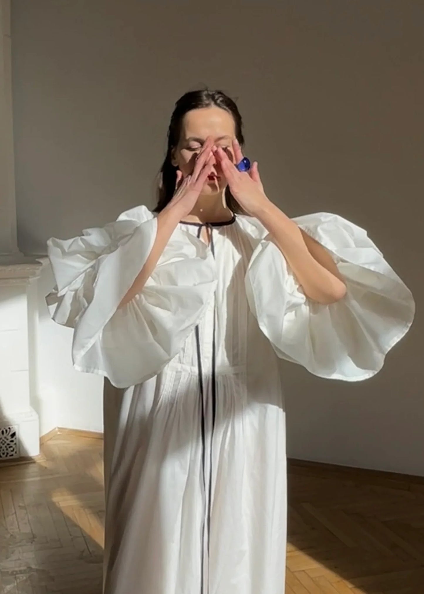 Model is wearing the Les Vacances d’Irina Favignana Dress in White, handcrafted from cotton and silk with multilayered sleeves and hand-sewn pleating, from the House of Nomad Stories selection.