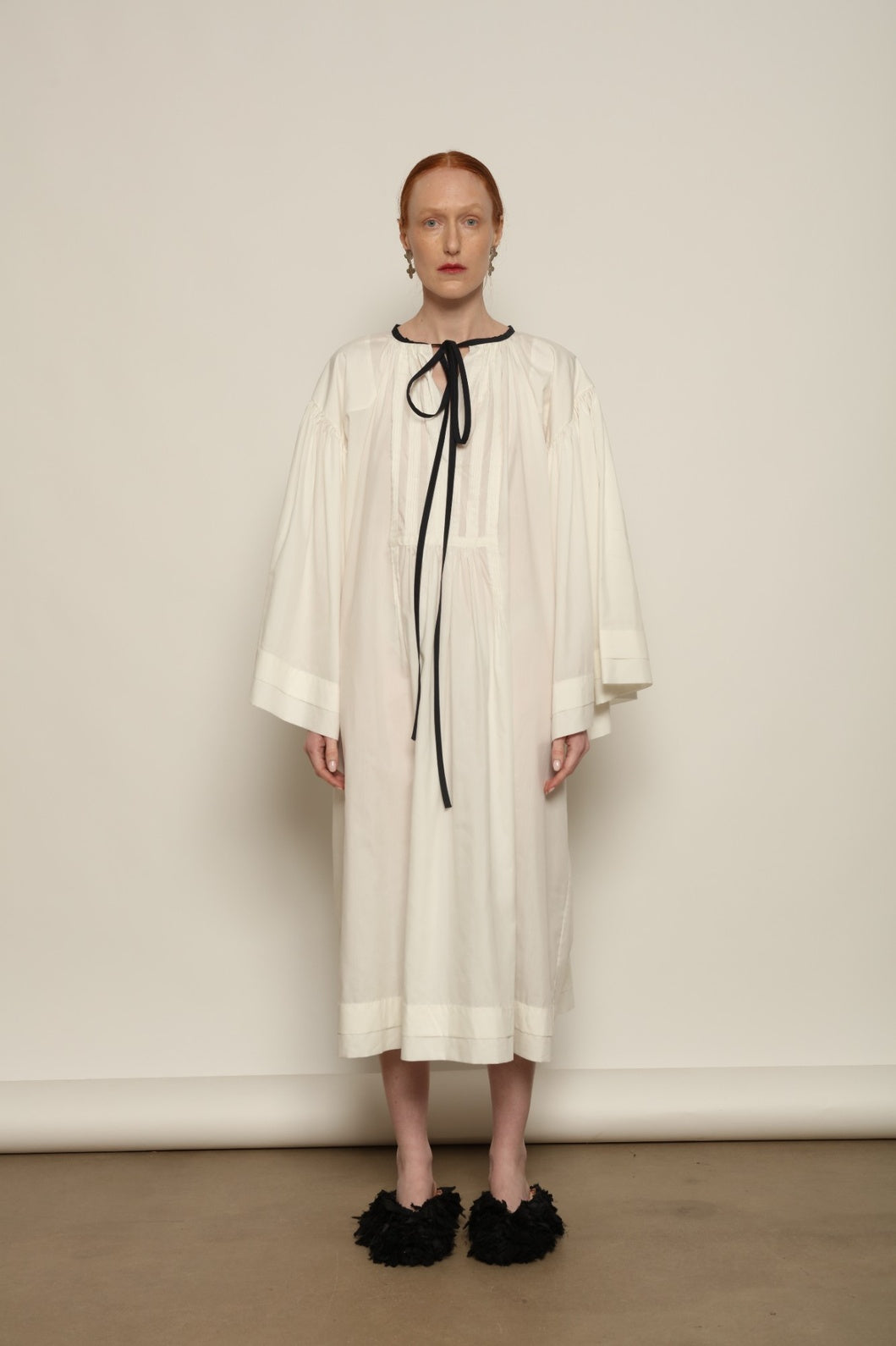 Model is wearing the Les Vacances d’Irina Favignana Dress in White, handcrafted from cotton and silk with multilayered sleeves and hand-sewn pleating, from the House of Nomad Stories selection.