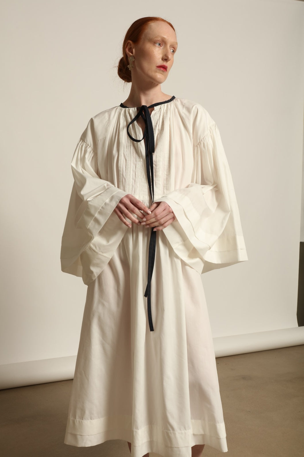 Model is wearing the Les Vacances d’Irina Favignana Dress in White, handcrafted from cotton and silk with multilayered sleeves and hand-sewn pleating, from the House of Nomad Stories selection.