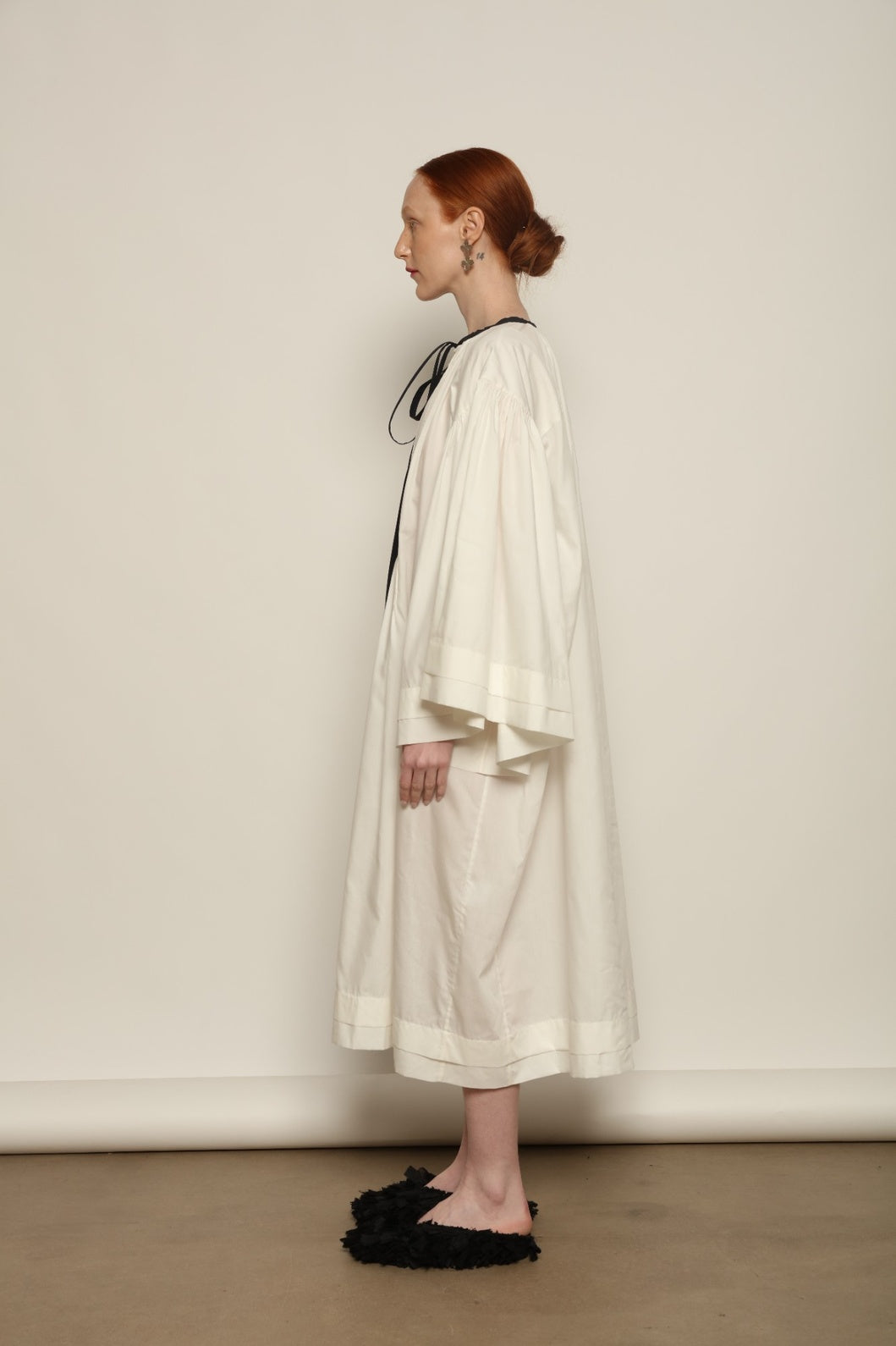 Model is wearing the Les Vacances d’Irina Favignana Dress in White, handcrafted from cotton and silk with multilayered sleeves and hand-sewn pleating, from the House of Nomad Stories selection.