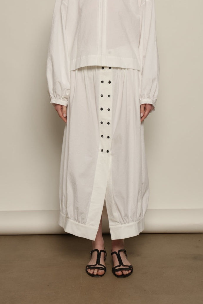 Model is wearing the Les Vacances d’Irina Jade white cotton skirt with high waist and double-breasted button front, from the House of Nomad Stories selection.