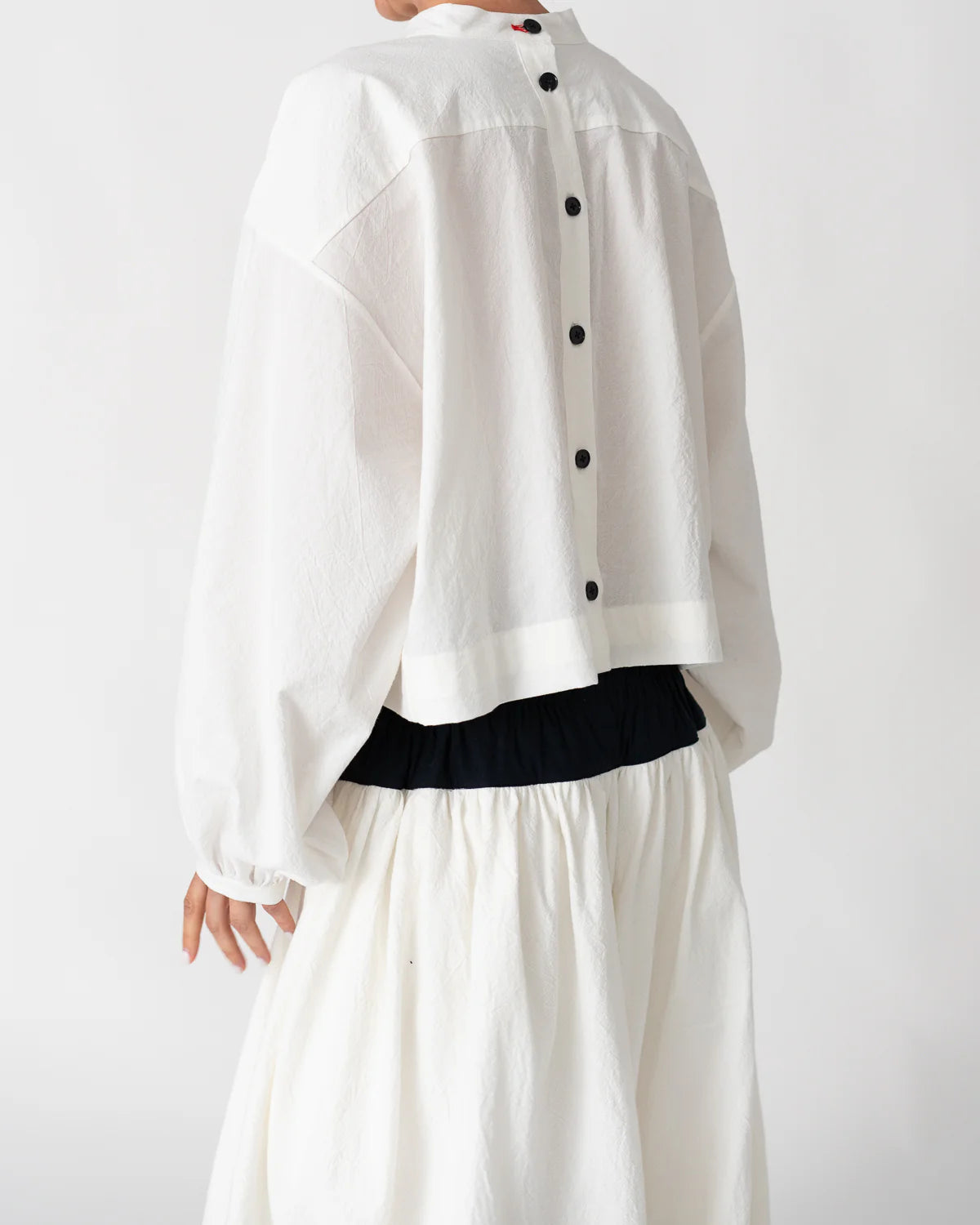 Model is wearing the Les Vacances d’Irina white cotton blouse in 100% cotton with voluminous sleeves and pleated front, from the House of Nomad Stories selection.