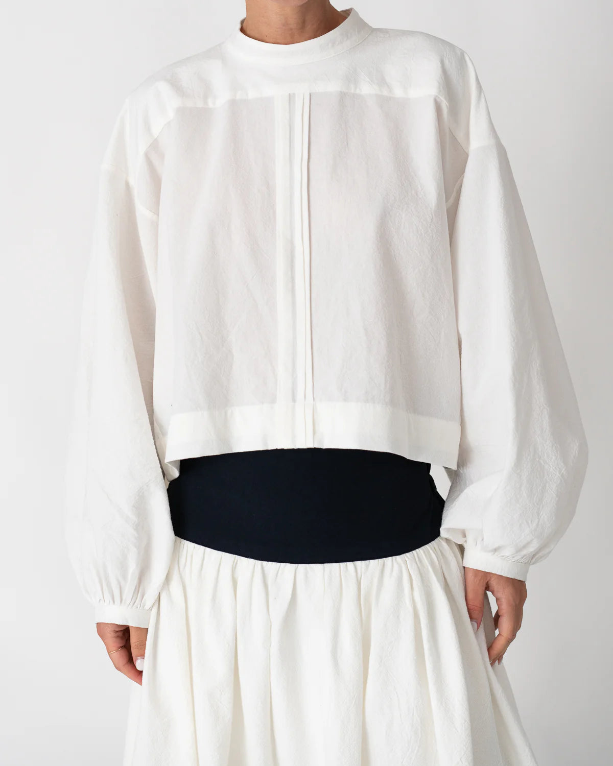Model is wearing the Les Vacances d’Irina white cotton blouse in 100% cotton with voluminous sleeves and pleated front, from the House of Nomad Stories selection.