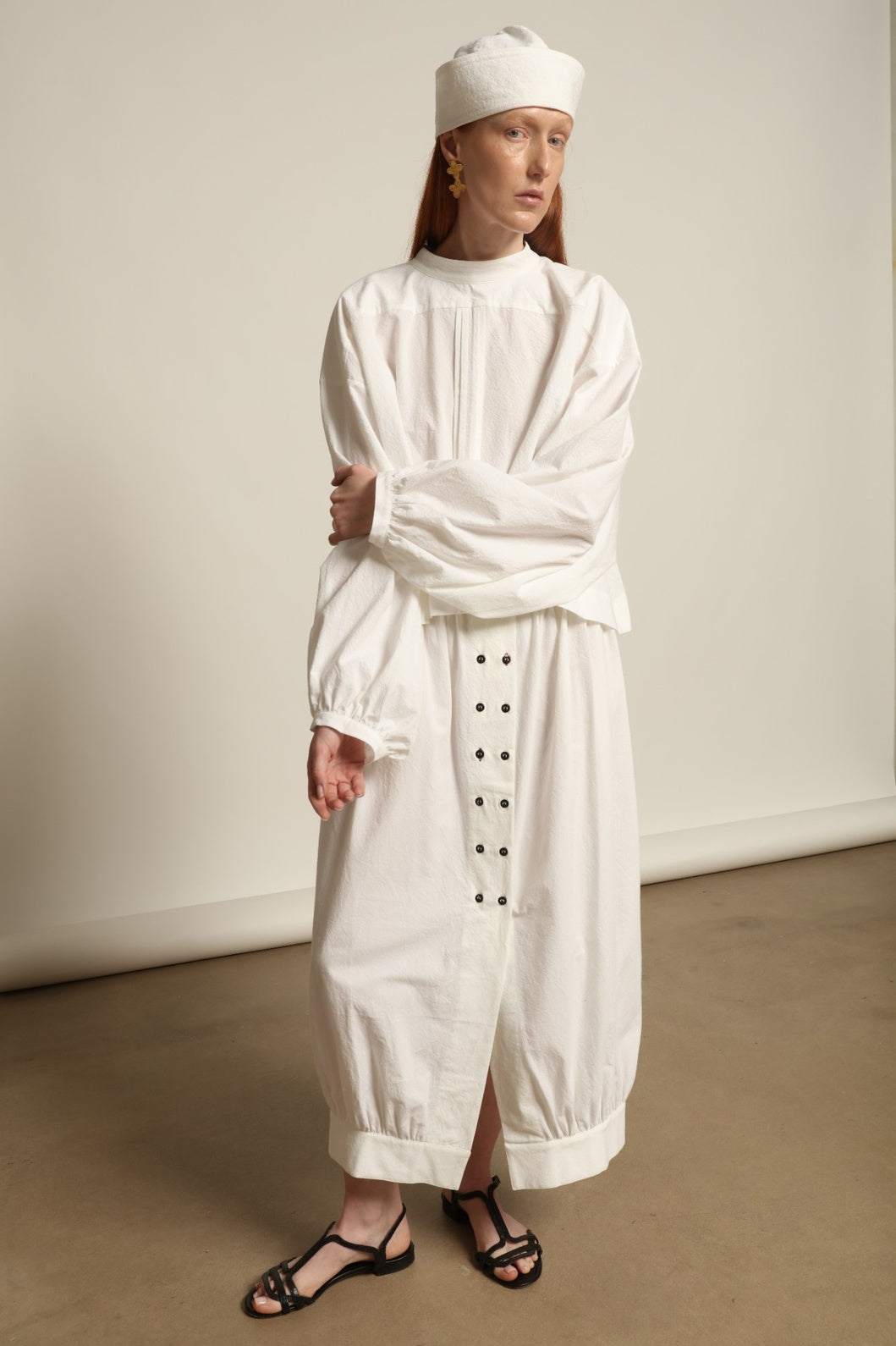 Model is wearing the Les Vacances d’Irina white cotton blouse in 100% cotton with voluminous sleeves and pleated front, from the House of Nomad Stories selection.