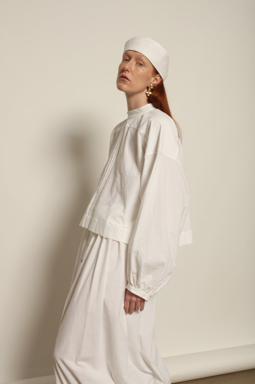 Model is wearing the Les Vacances d’Irina white cotton blouse in 100% cotton with voluminous sleeves and pleated front, from the House of Nomad Stories selection.