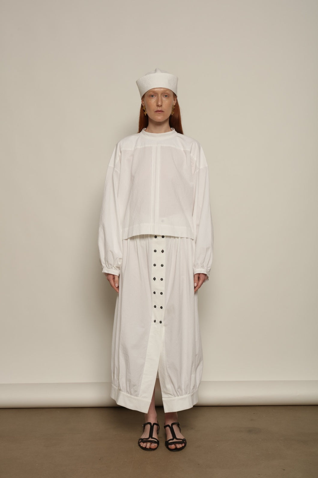 Model is wearing the Les Vacances d’Irina white cotton blouse in 100% cotton with voluminous sleeves and pleated front, from the House of Nomad Stories selection.