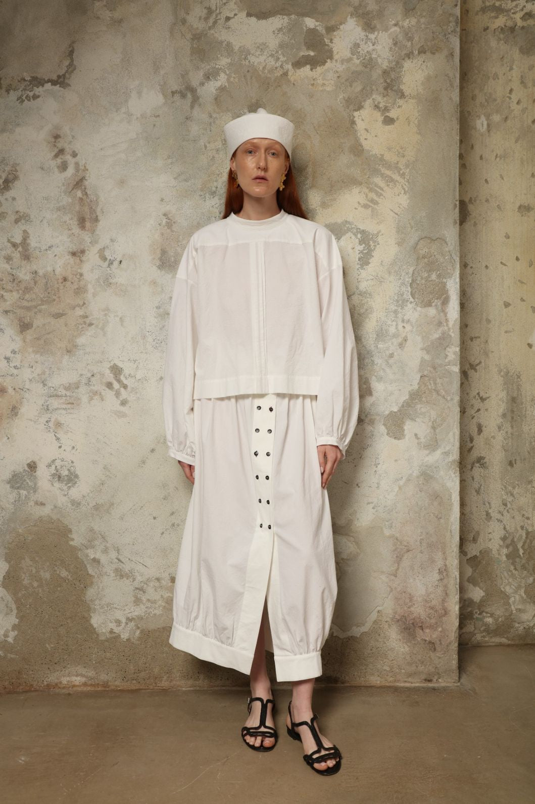Model is wearing the Les Vacances d’Irina white cotton blouse in 100% cotton with voluminous sleeves and pleated front, from the House of Nomad Stories selection.