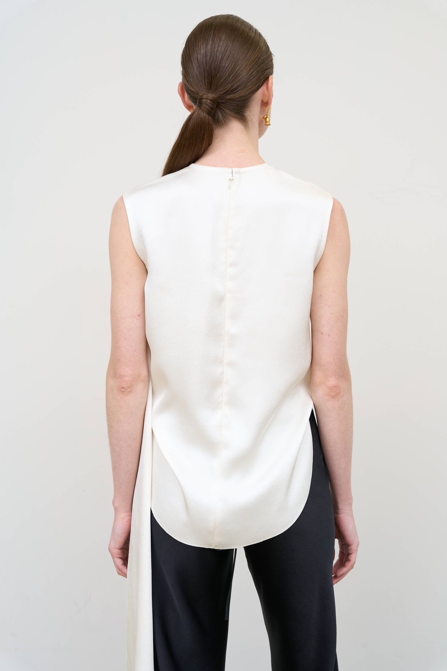 Model is wearing an asymmetric white twist top by Litkovska with sculptural draping and sleeveless design, modern designer top available at House of Woven Stories