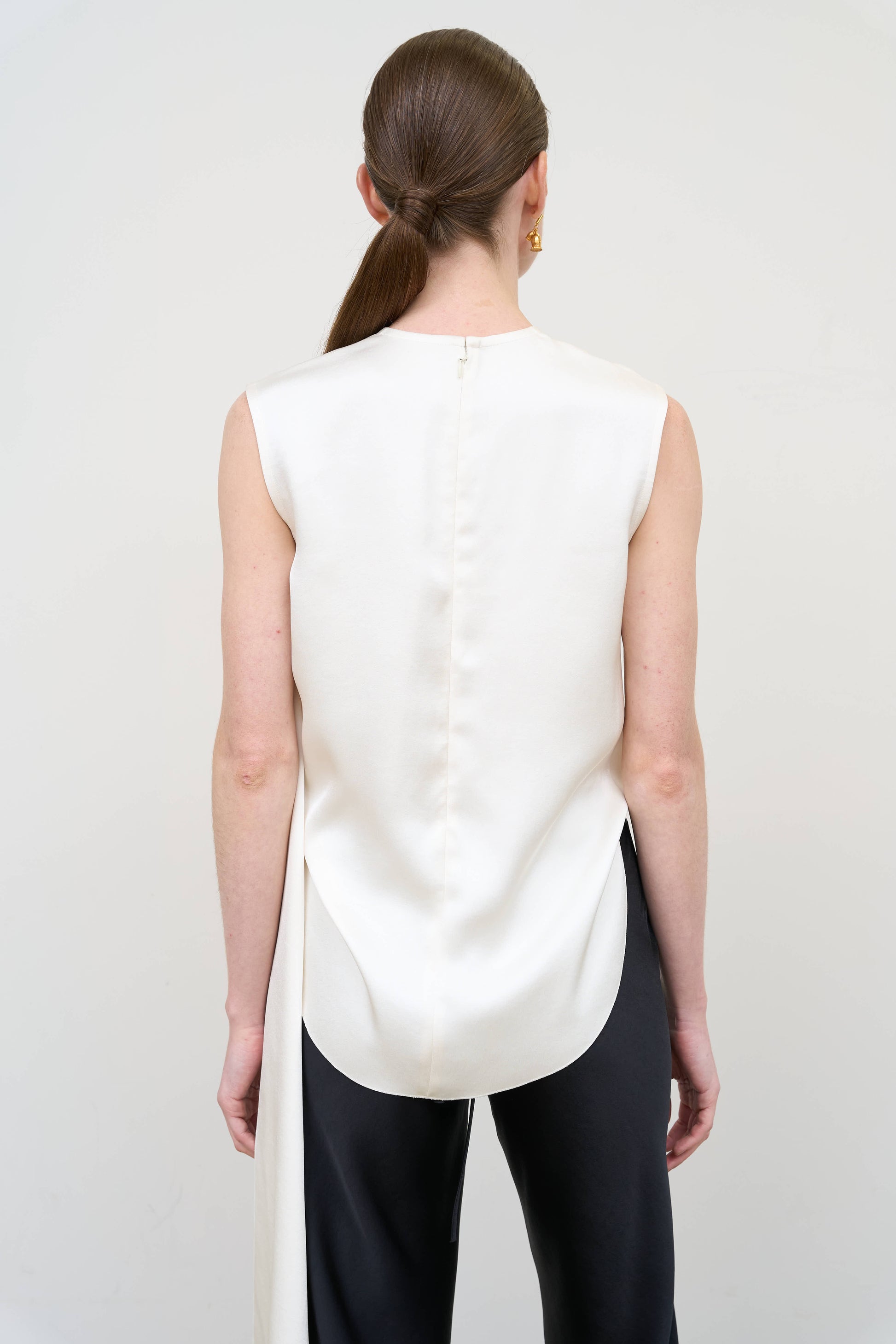 Model is wearing an asymmetric white twist top by Litkovska with sculptural draping and sleeveless design, modern designer top available at House of Woven Stories