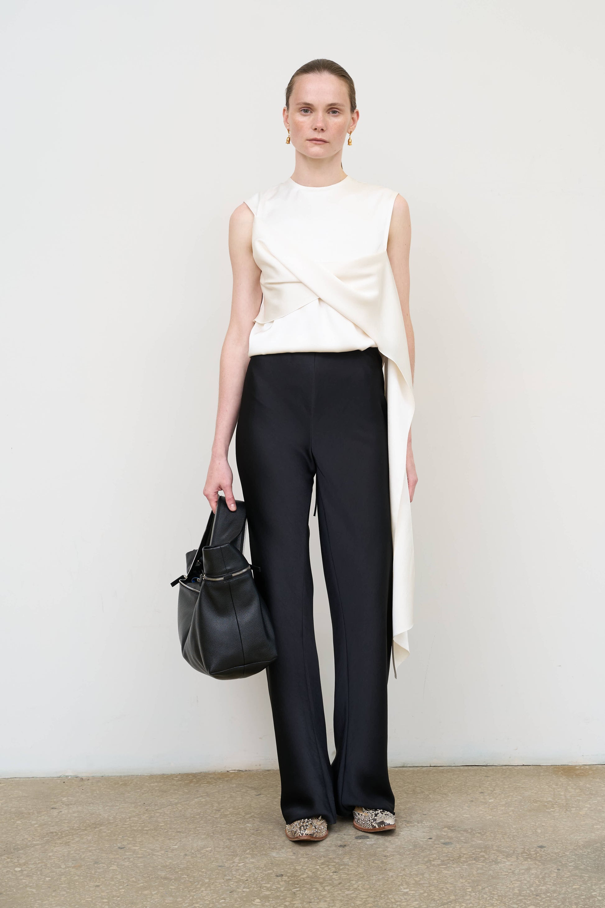 Model is wearing an asymmetric white twist top by Litkovska with sculptural draping and sleeveless design, modern designer top available at House of Woven Stories