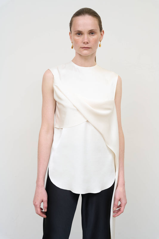 Model is wearing an asymmetric white twist top by Litkovska with sculptural draping and sleeveless design, modern designer top available at House of Woven Stories